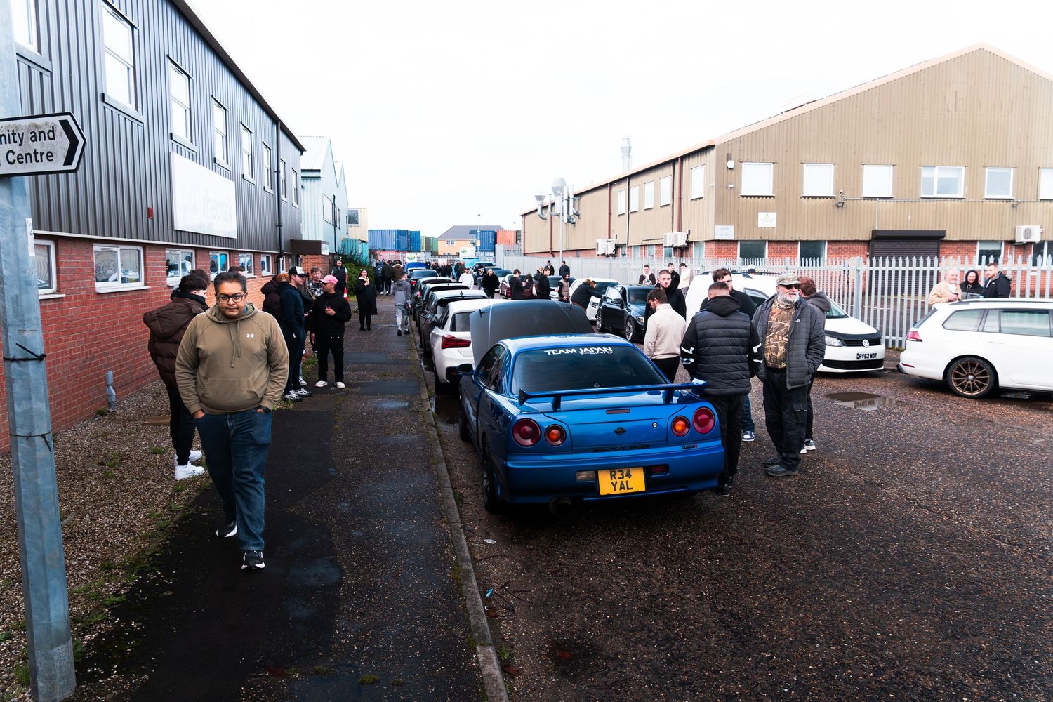 Car enthusiasts gathered at UK industrial estate car meet with blue Nissan GT-R in foreground.