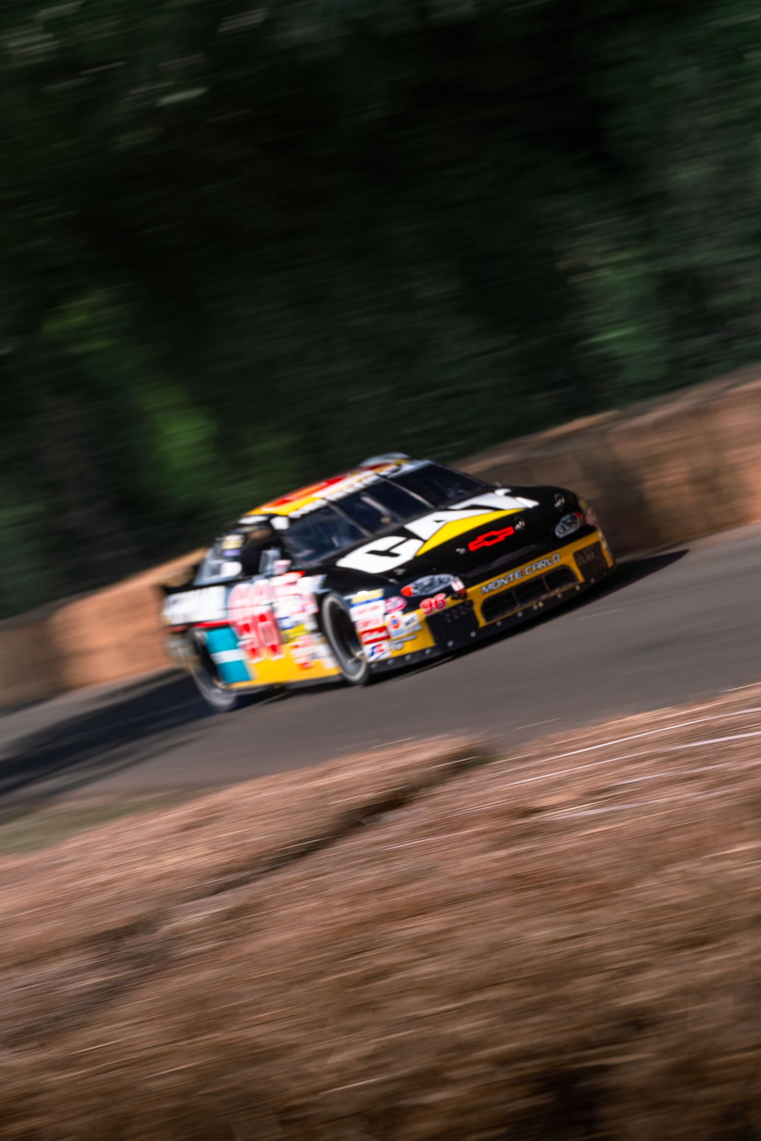 A black NASCAR race car with CAT sponsorship speeds along a winding road course, motion blur emphasizing its velocity.