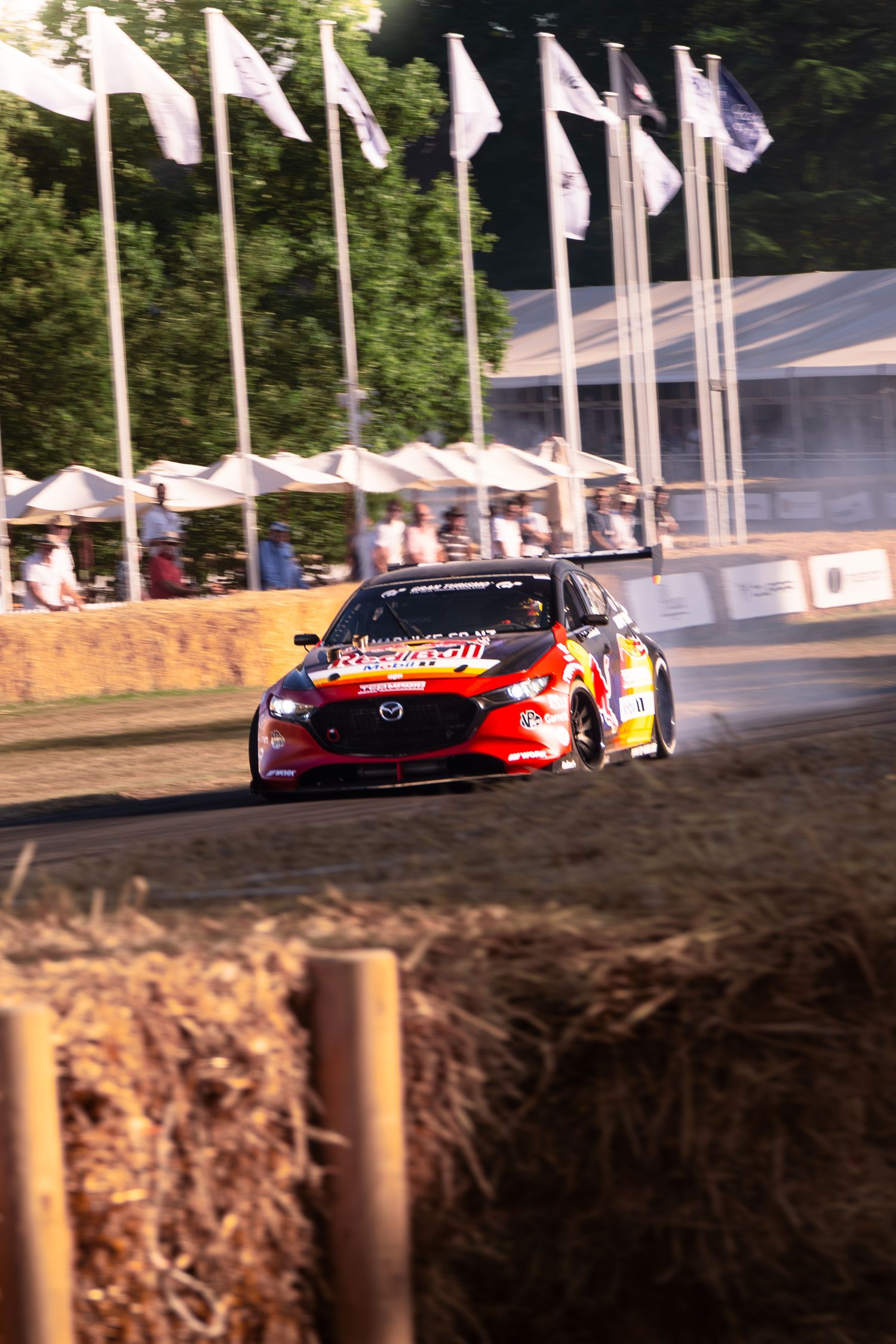 Red Bull racing car drifting on hillclimb course at Goodwood Festival of Speed with flags and spectators.