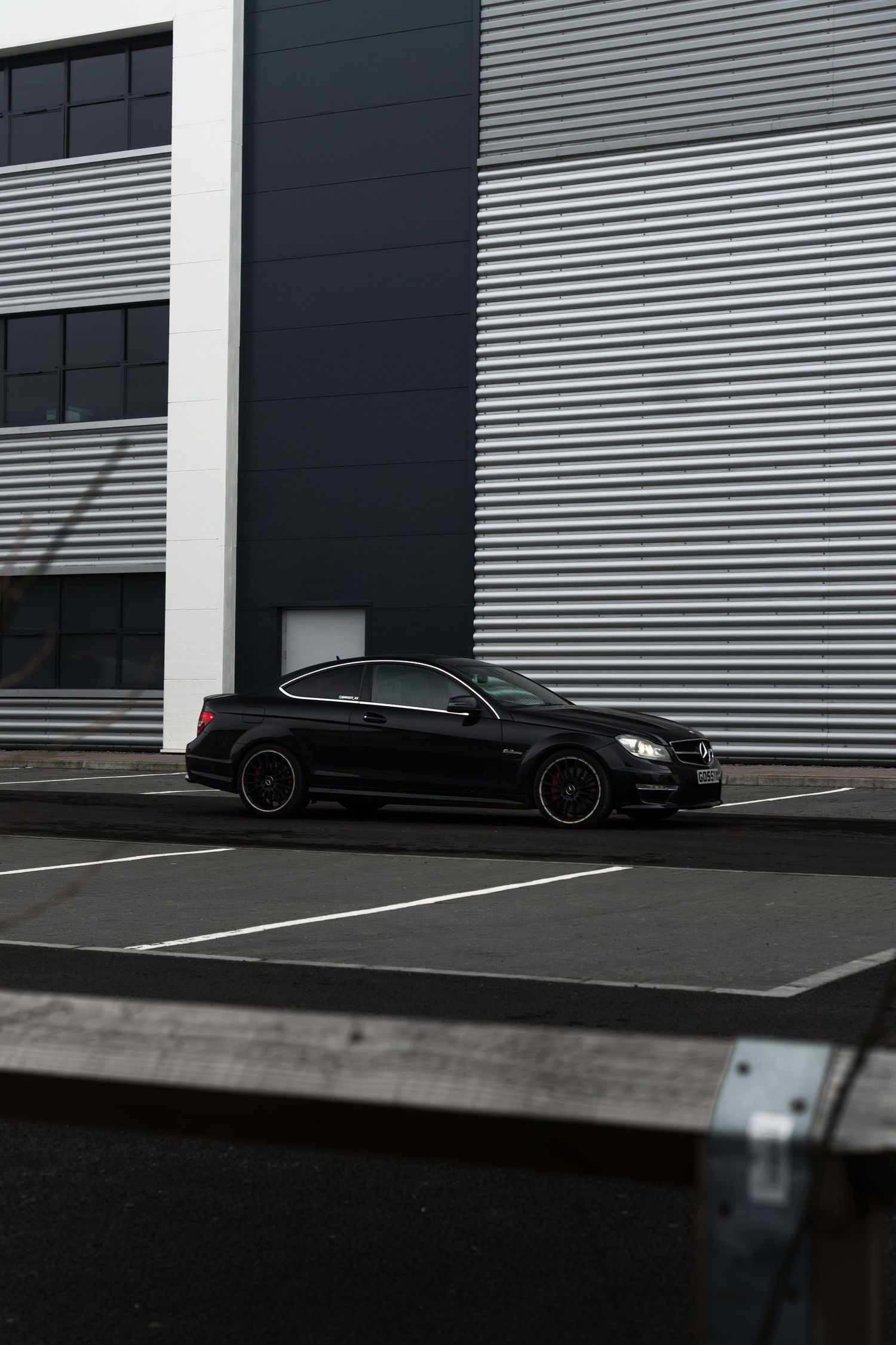 Black Mercedes-AMG C63 coupe parked in front of a corrugated metal industrial building.