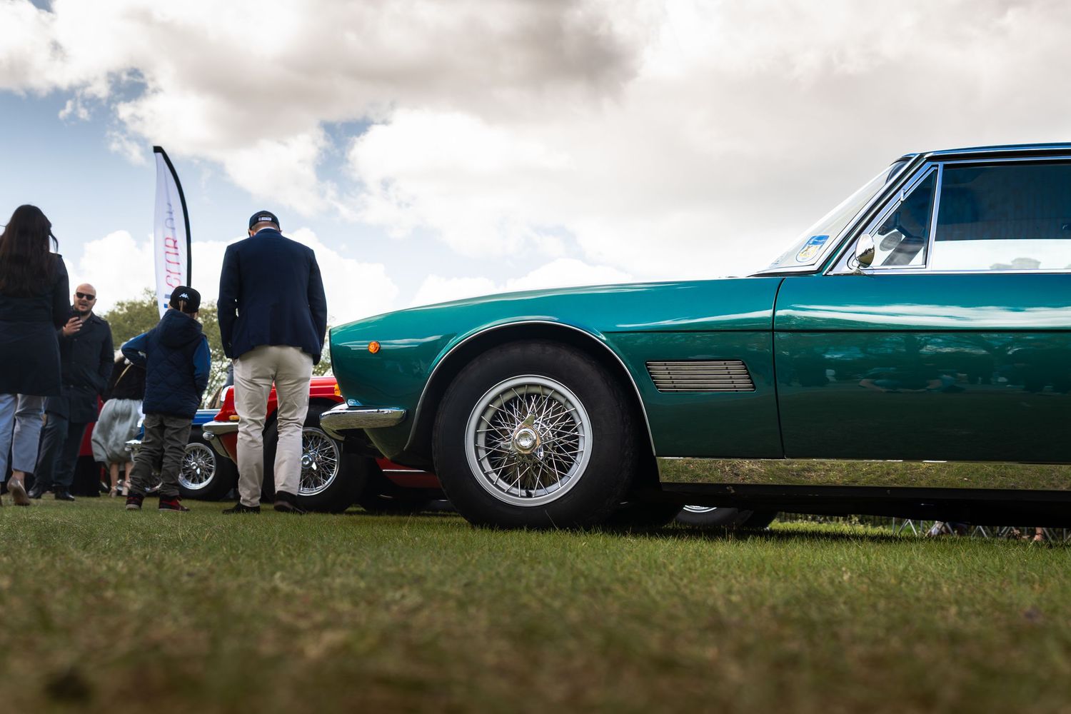 Classic green vintage car with wire wheels on display at an outdoor car show with spectators nearby.