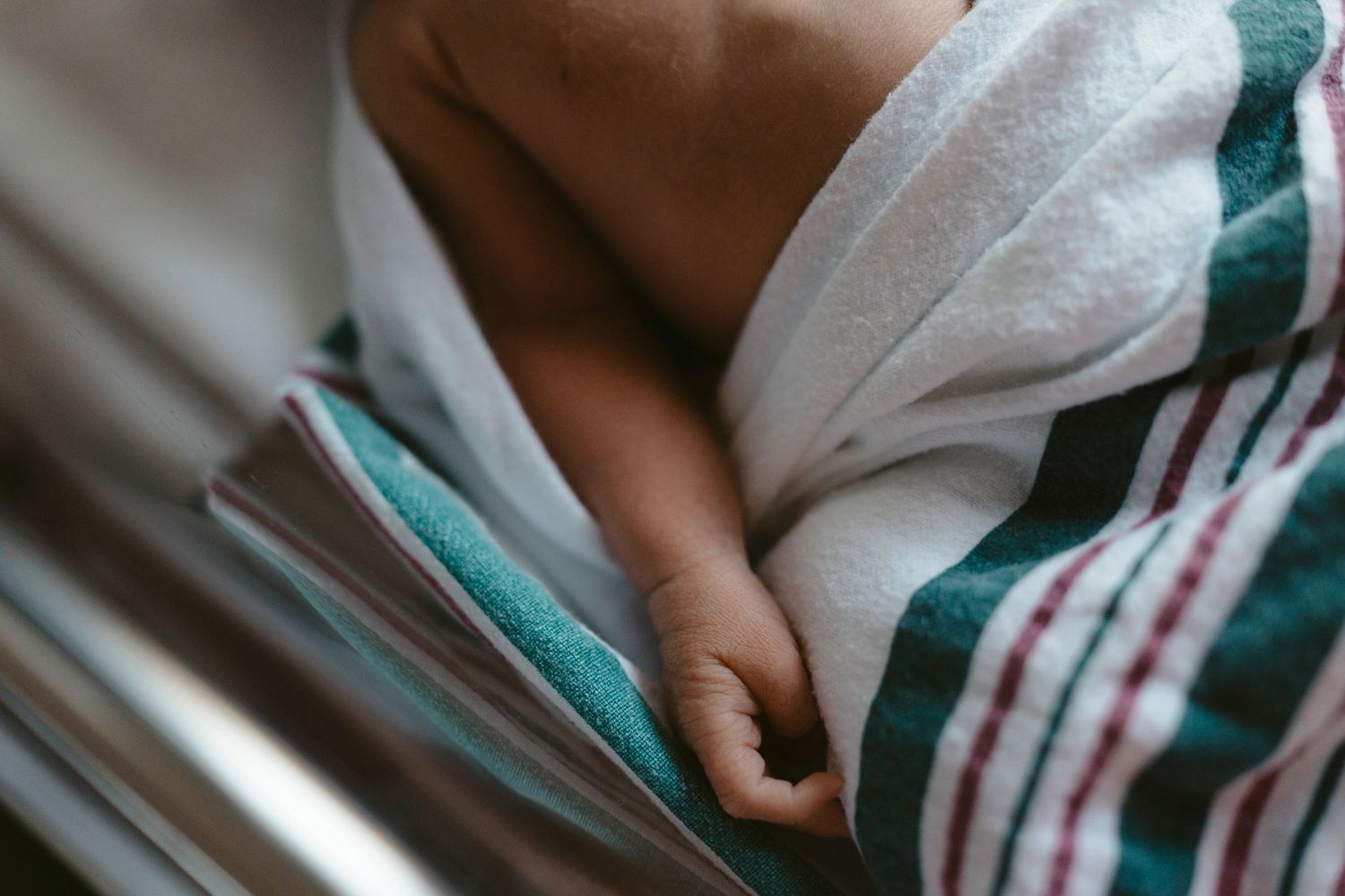 Close up view of hands holding a book while wrapped in a white and green striped blanket.