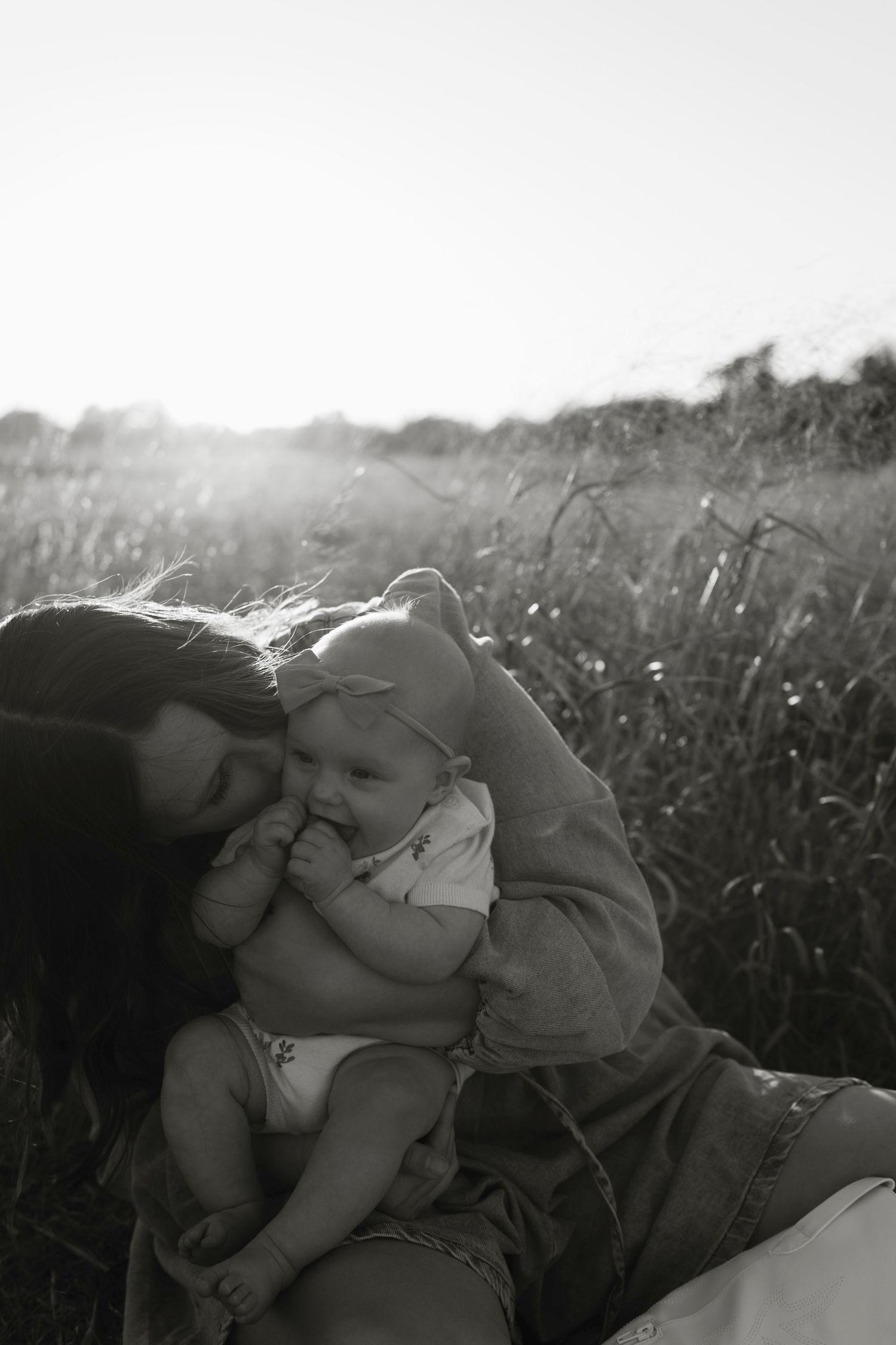 Tender black and white imagery captures affectionate moment between mother and child reclining in a grassy field in the greater Austin area.