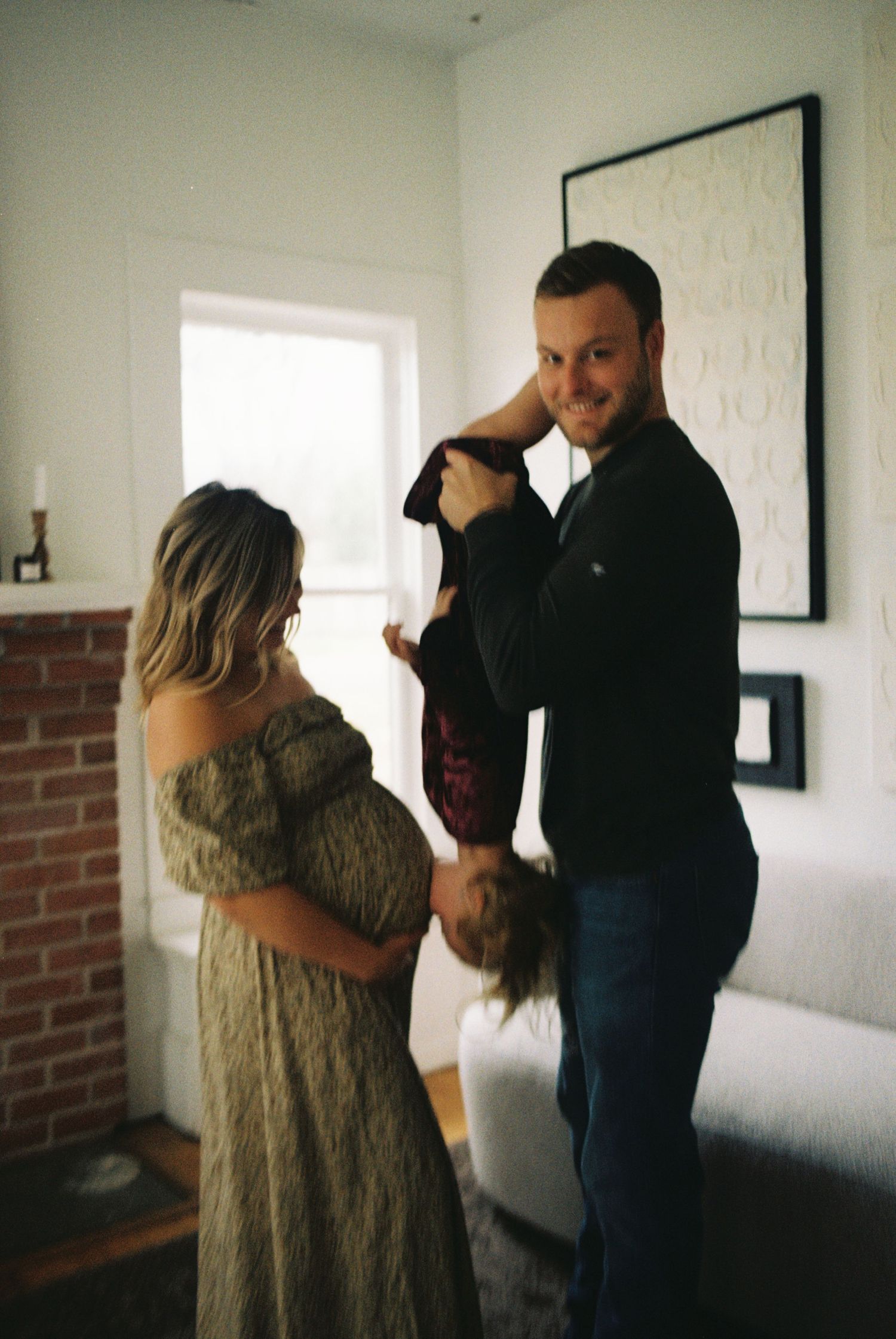 A couple shares an intimate dance together in a sunlit room with white walls and exposed brick.
