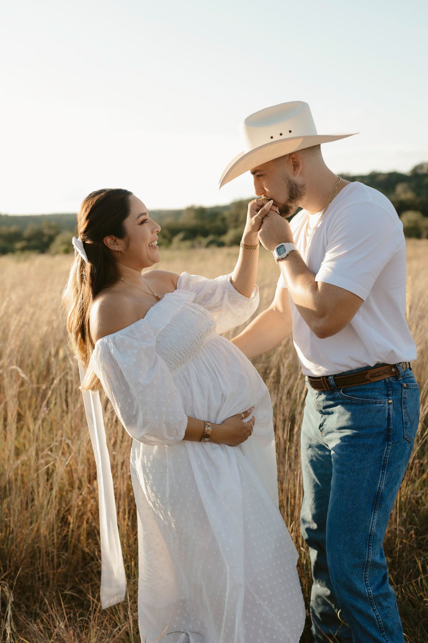 A romantic maternity photoshoot in a golden wheat field at sunset shows a couple sharing a tender moment.