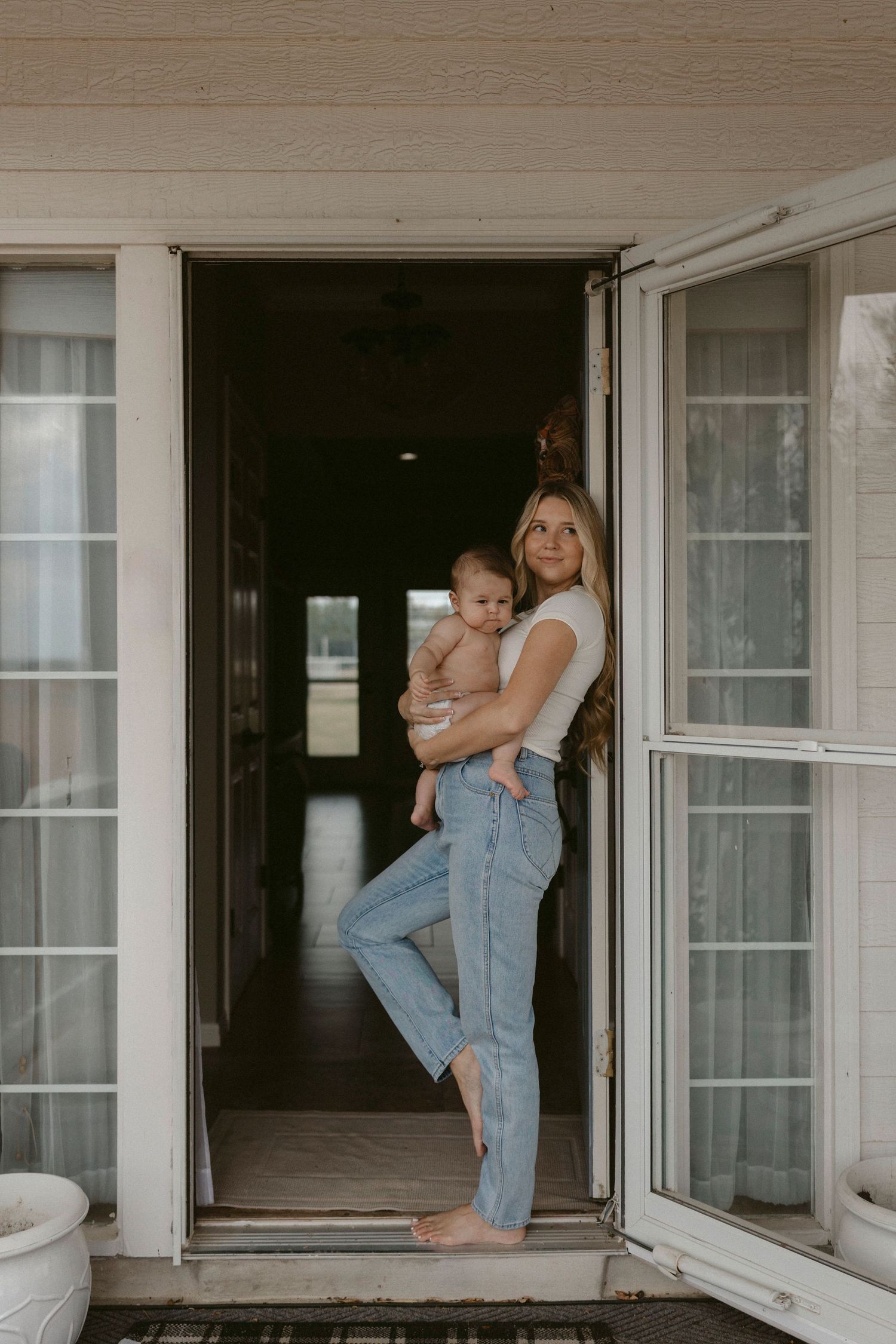 Motherhood photo of a mom holding her baby on the front porch, framed in the doorway of their home.