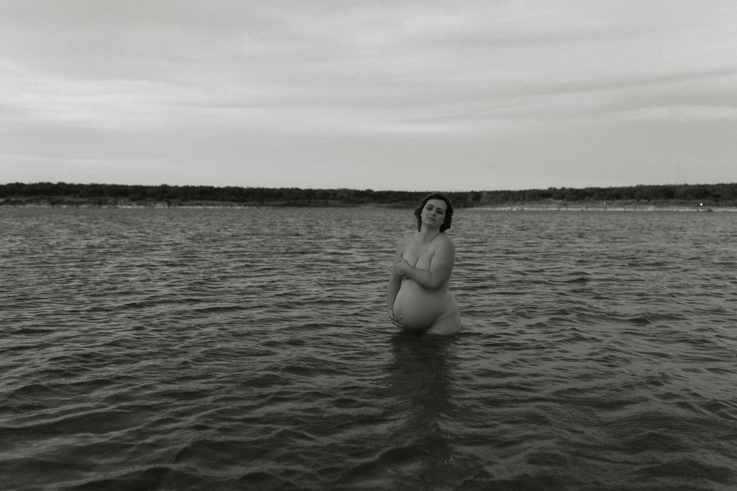 A black and white maternity portrait of a nude mother in the Austin, Texas area in the still waters of a local lake.