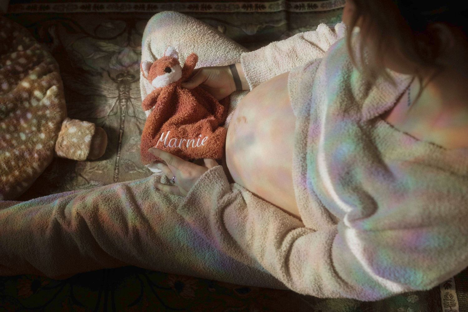 A pregnant mother sitting on the floor holding a red lovie