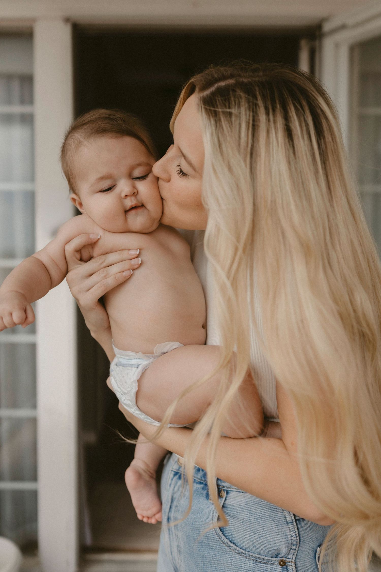 Tender motherhood moment of a mom kissing her baby during an in-home documentary session.