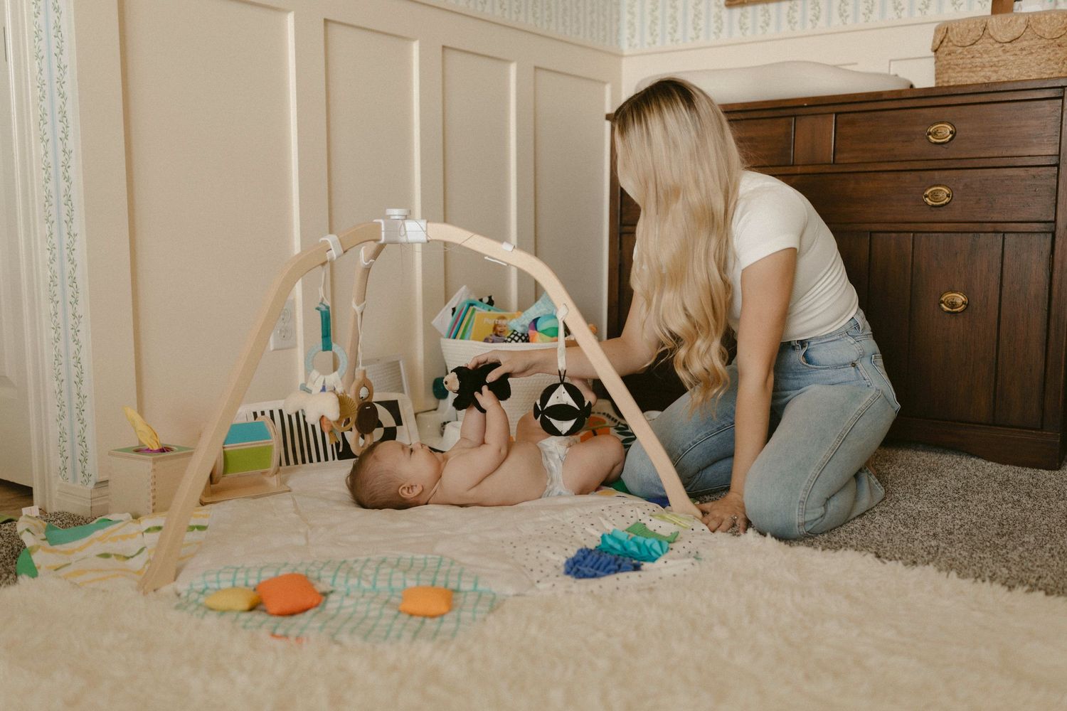 A person sits on a carpeted floor playing with colorful toys with baby and blocks in a home setting.