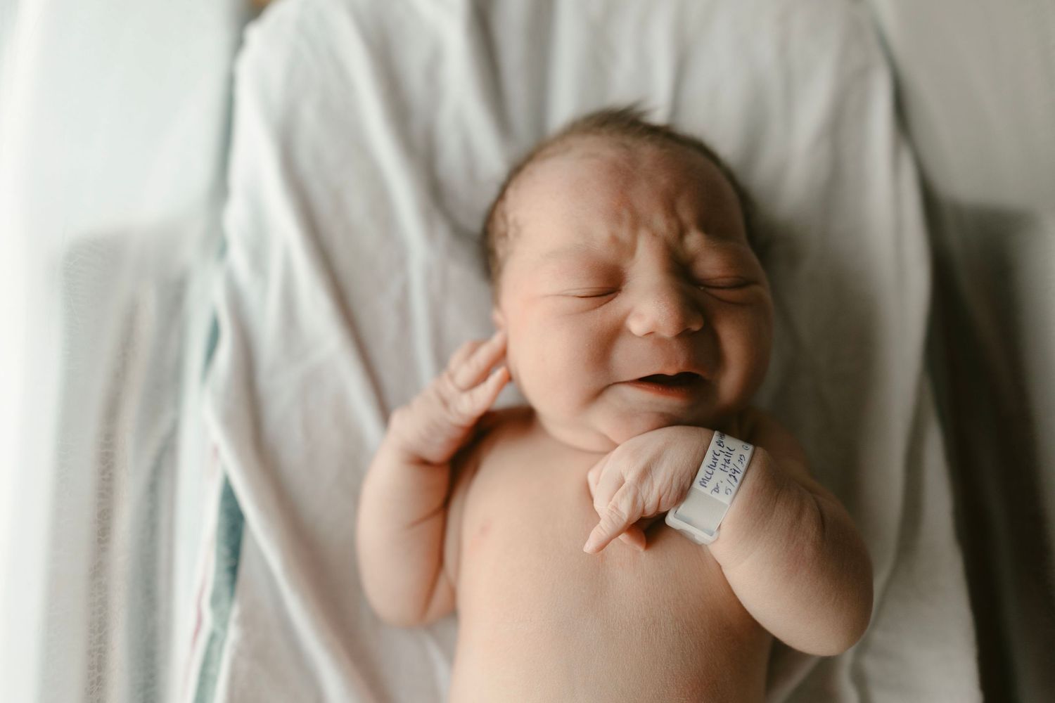 A newborn baby showing tiny hands, feet, and sleeping poses against soft white fabric.