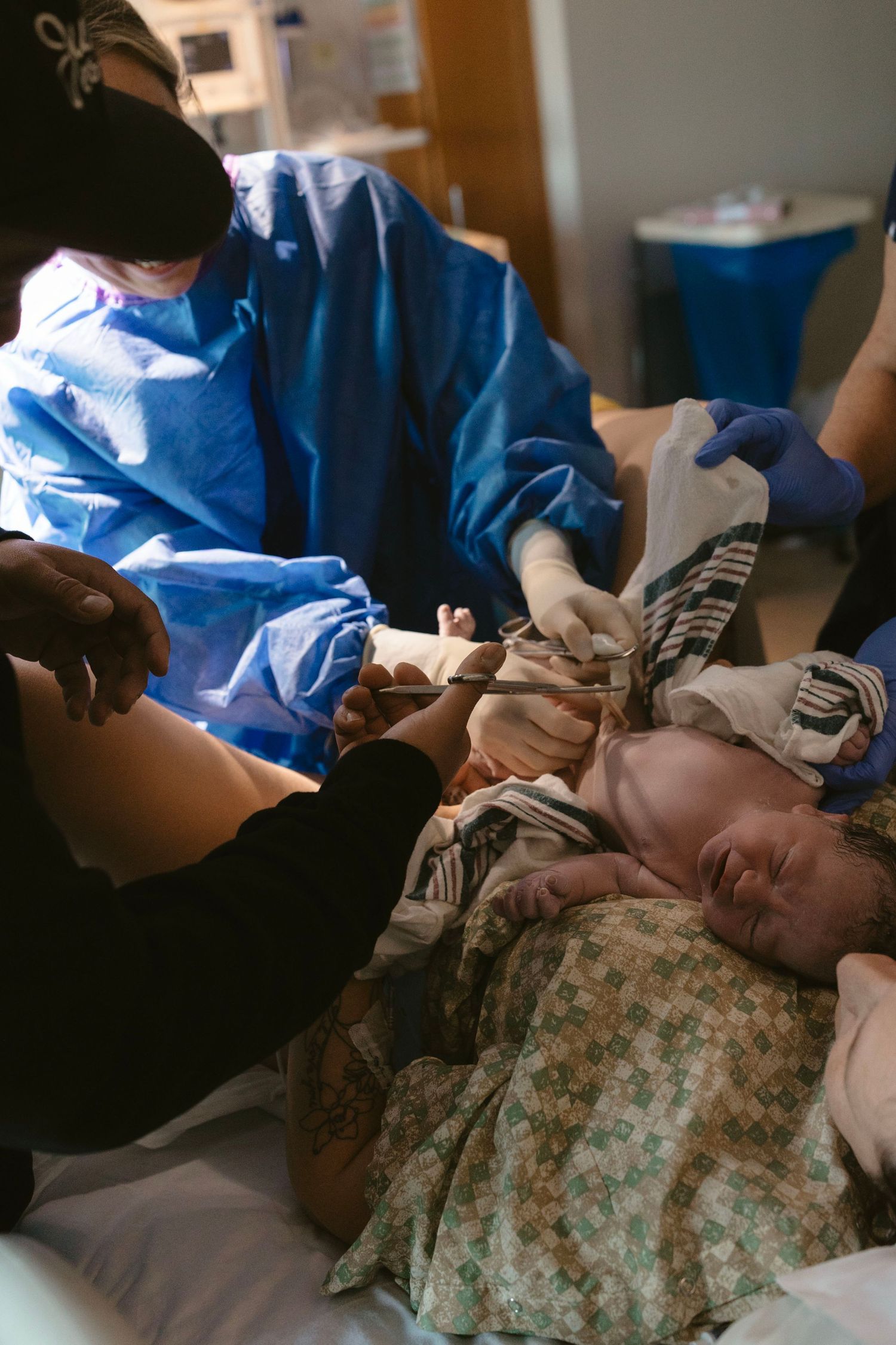 Birth photography capturing a father cutting the cord during the first moments after birth.