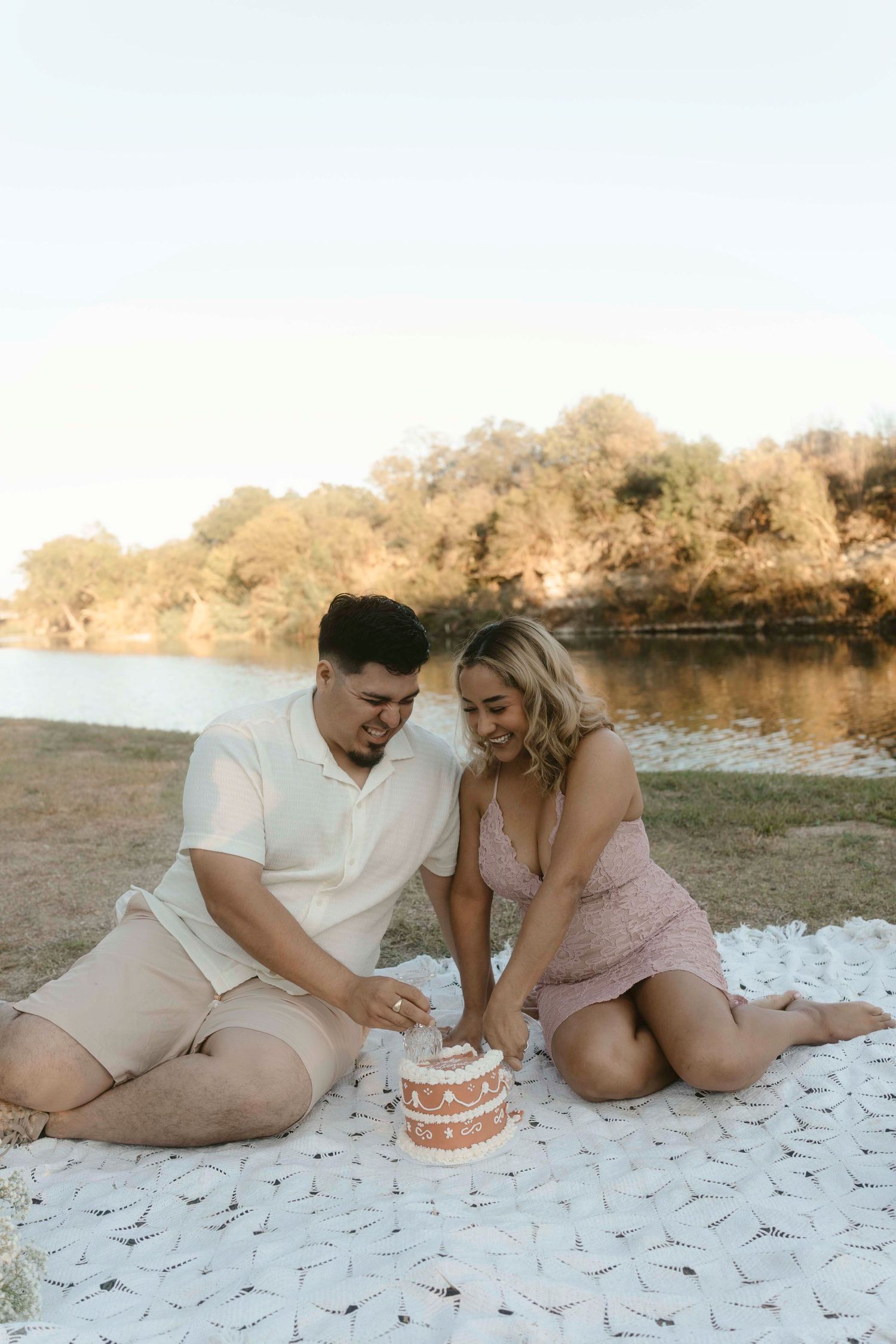 Couple sharing sweet moments on a picnic blanket by a lakeside during sunset.
