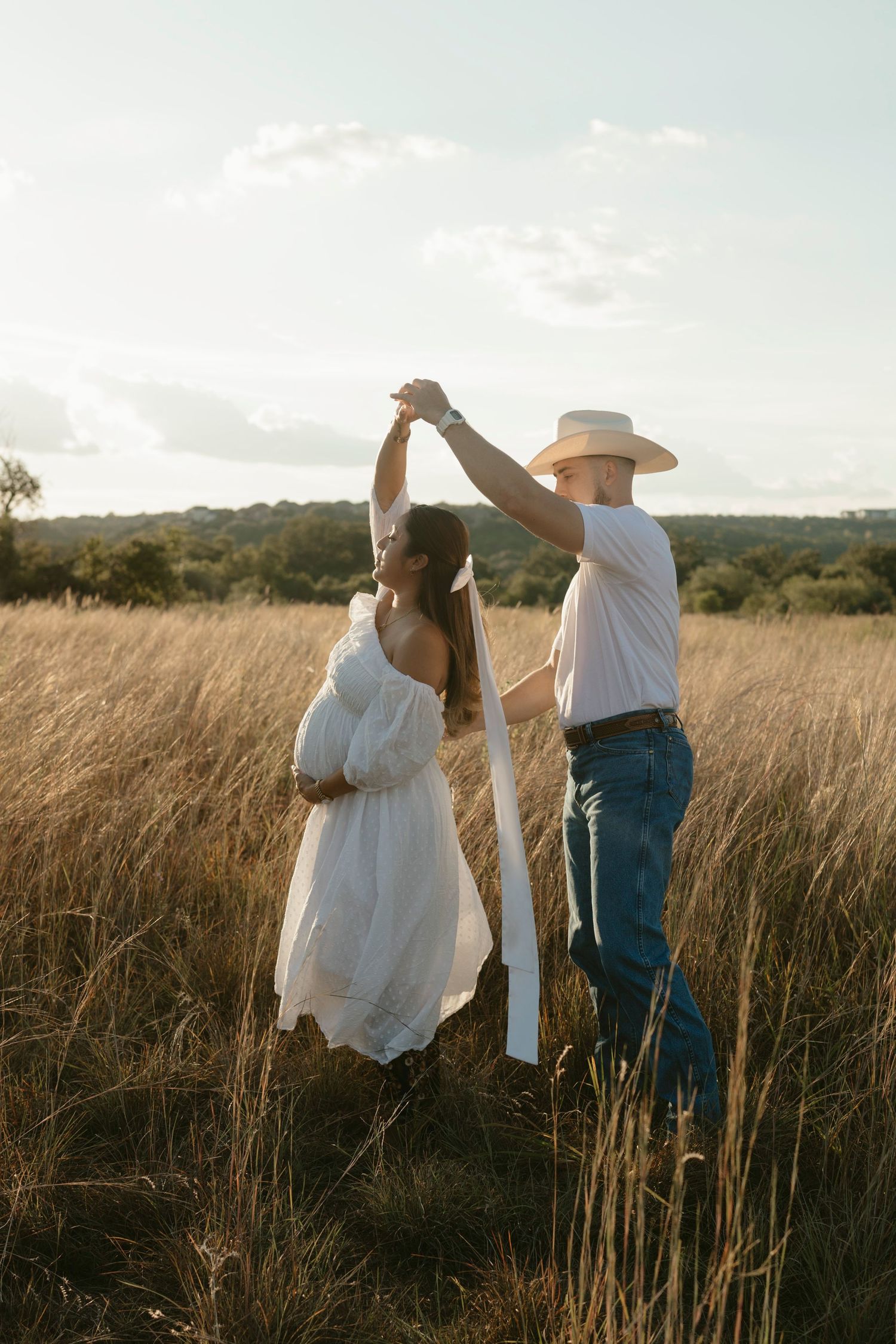 A couple dances together in a golden wheat field during sunset, creating a romantic silhouette against the landscape.