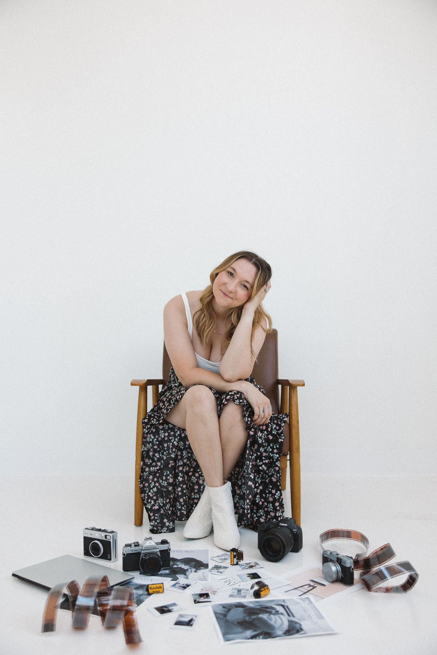 A series of photos showing a person in a floral dress sitting in a wooden chair with vintage cameras and photographs scattered around.
