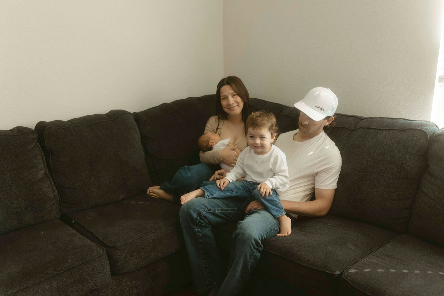 A family lies on a gray couch in a dimly lit living room.
