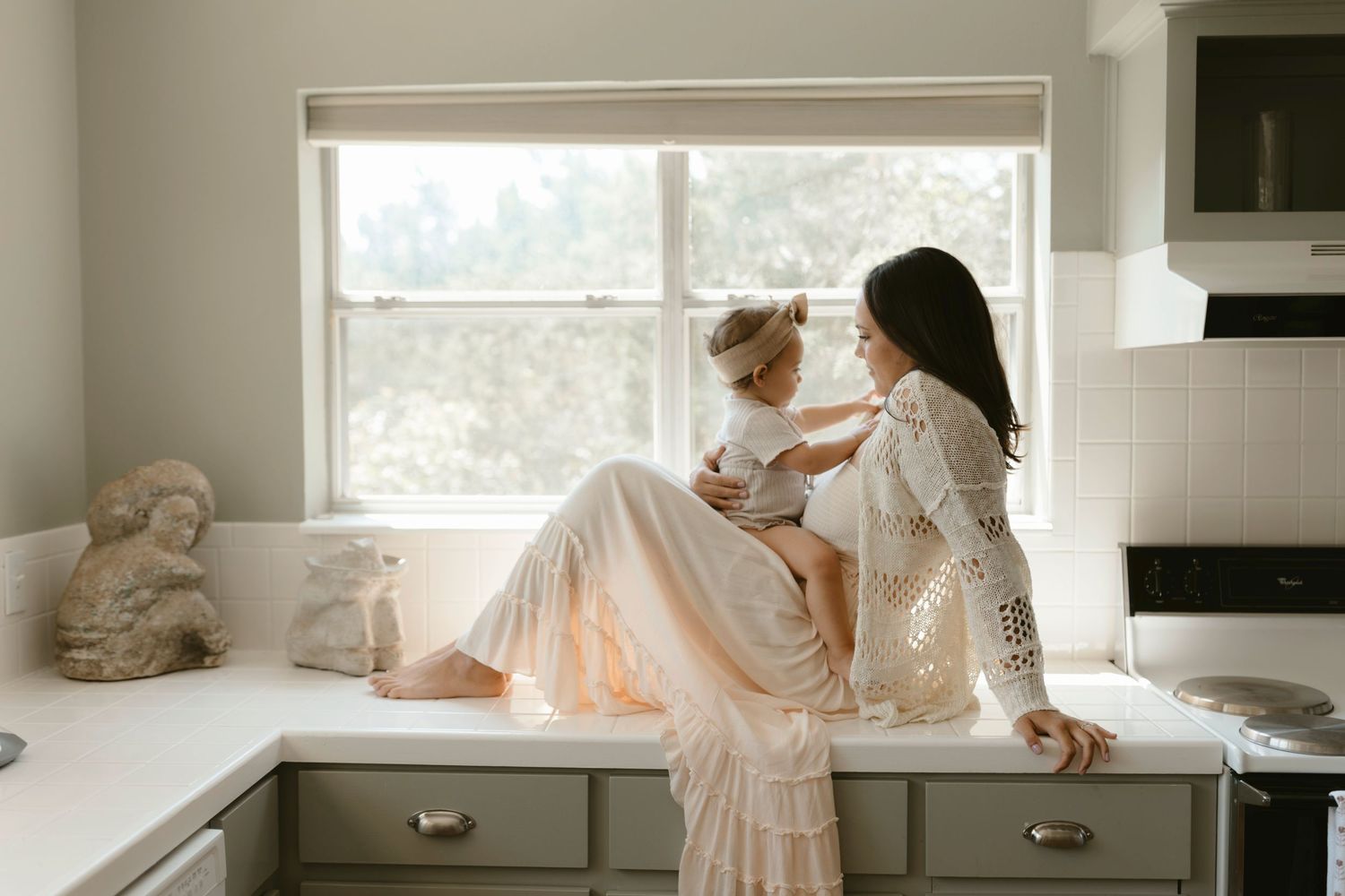 Tender photography moment shared in soft window light as mother and child bond in the kitchen.