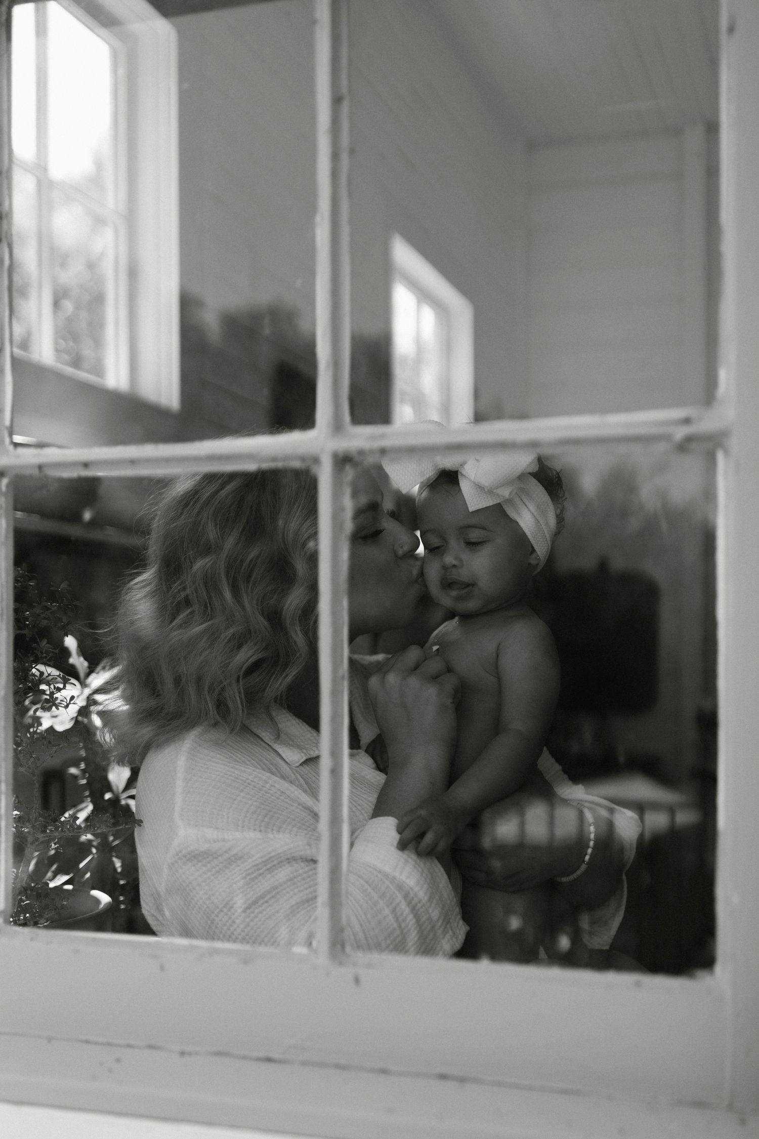 Black and white window view of tender motherhood moment through paned glass by Brittany Ruiz Photography in Austin, TX.