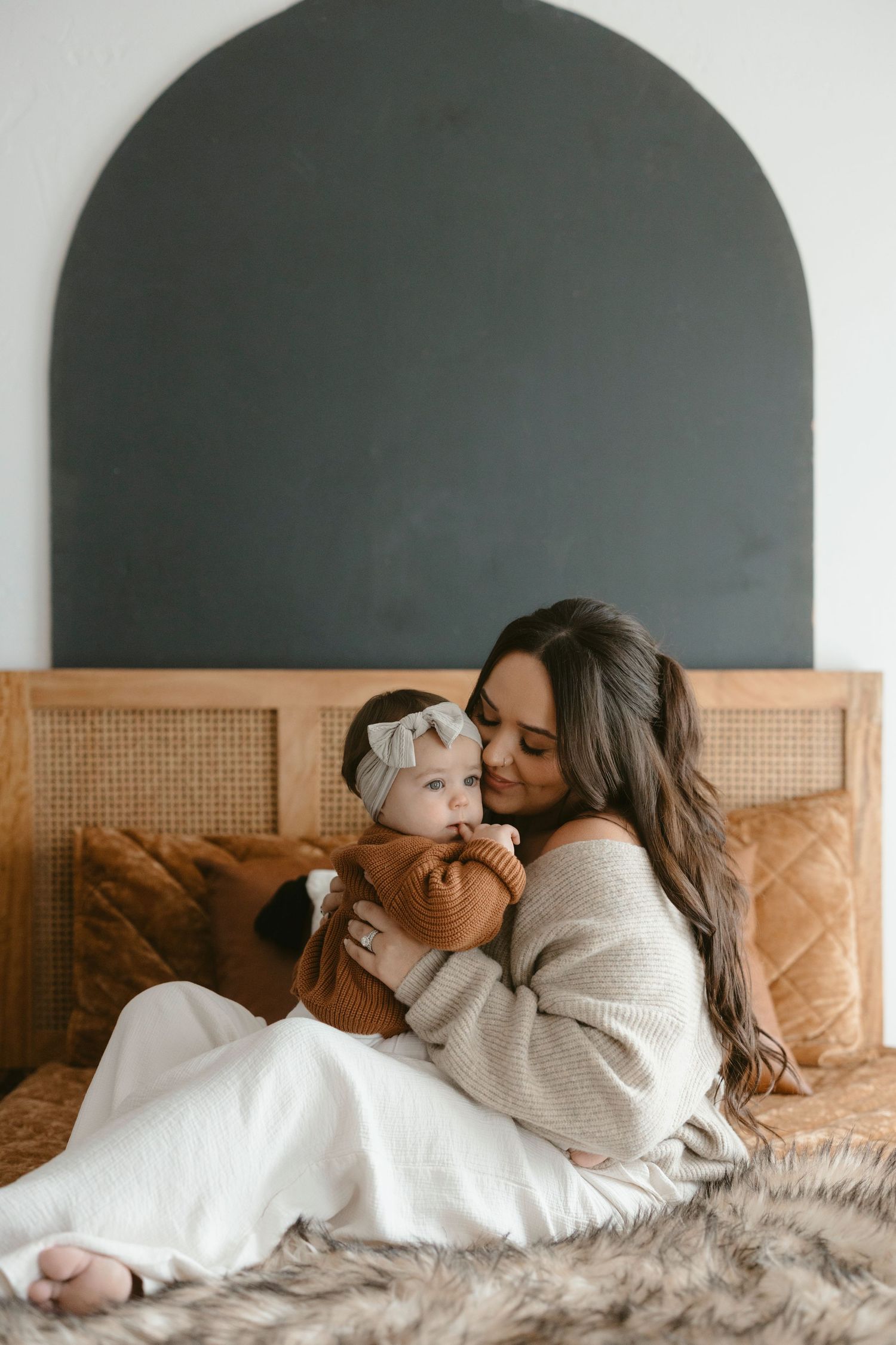 Intimate moment of parent and baby cuddling on bed with rattan headboard and dark arch wall in the Austin, Texas area.
