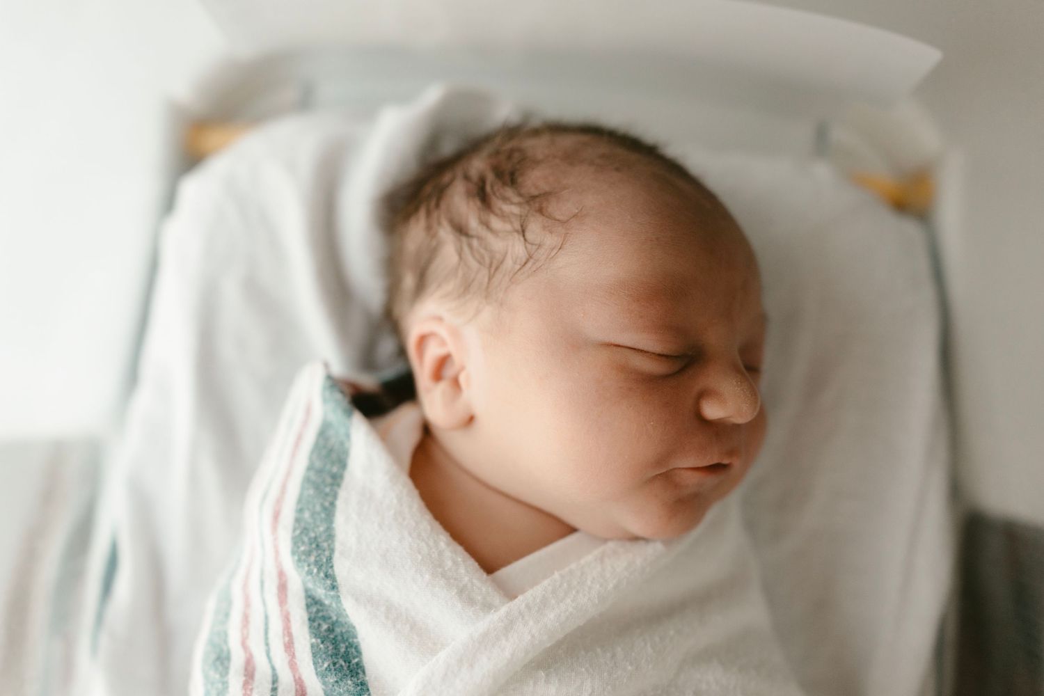 A peaceful newborn baby in Austin, Texas sleeps soundly while swaddled in a white blanket.