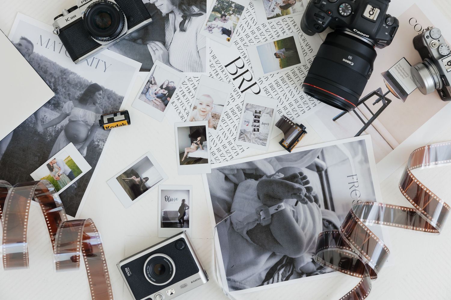 Vintage cameras and assorted black and white photographs scattered across a white surface in an artistic layout.
