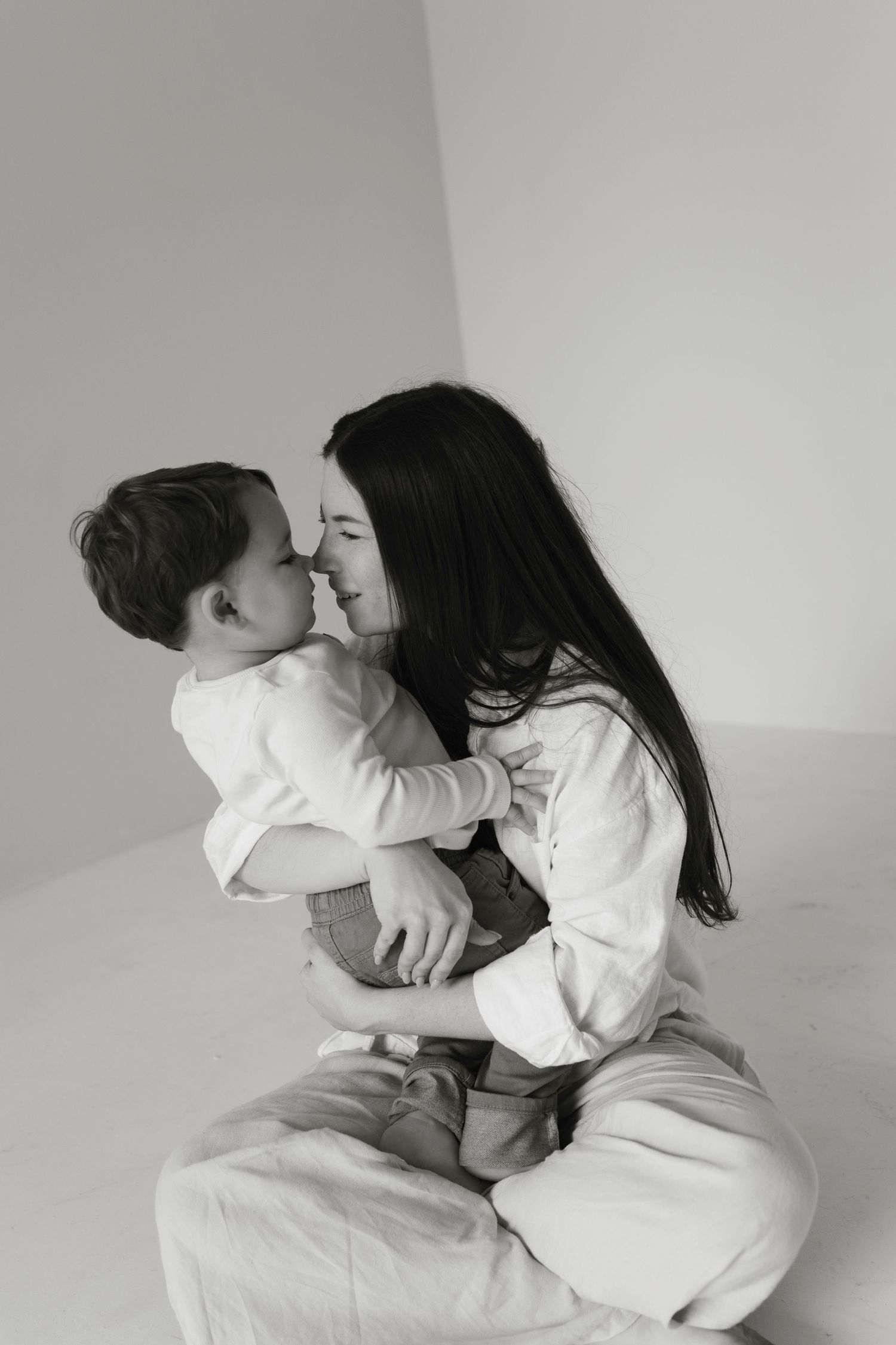 Mom and tollder sitting on the ground with their noses touching in  a black and white photo