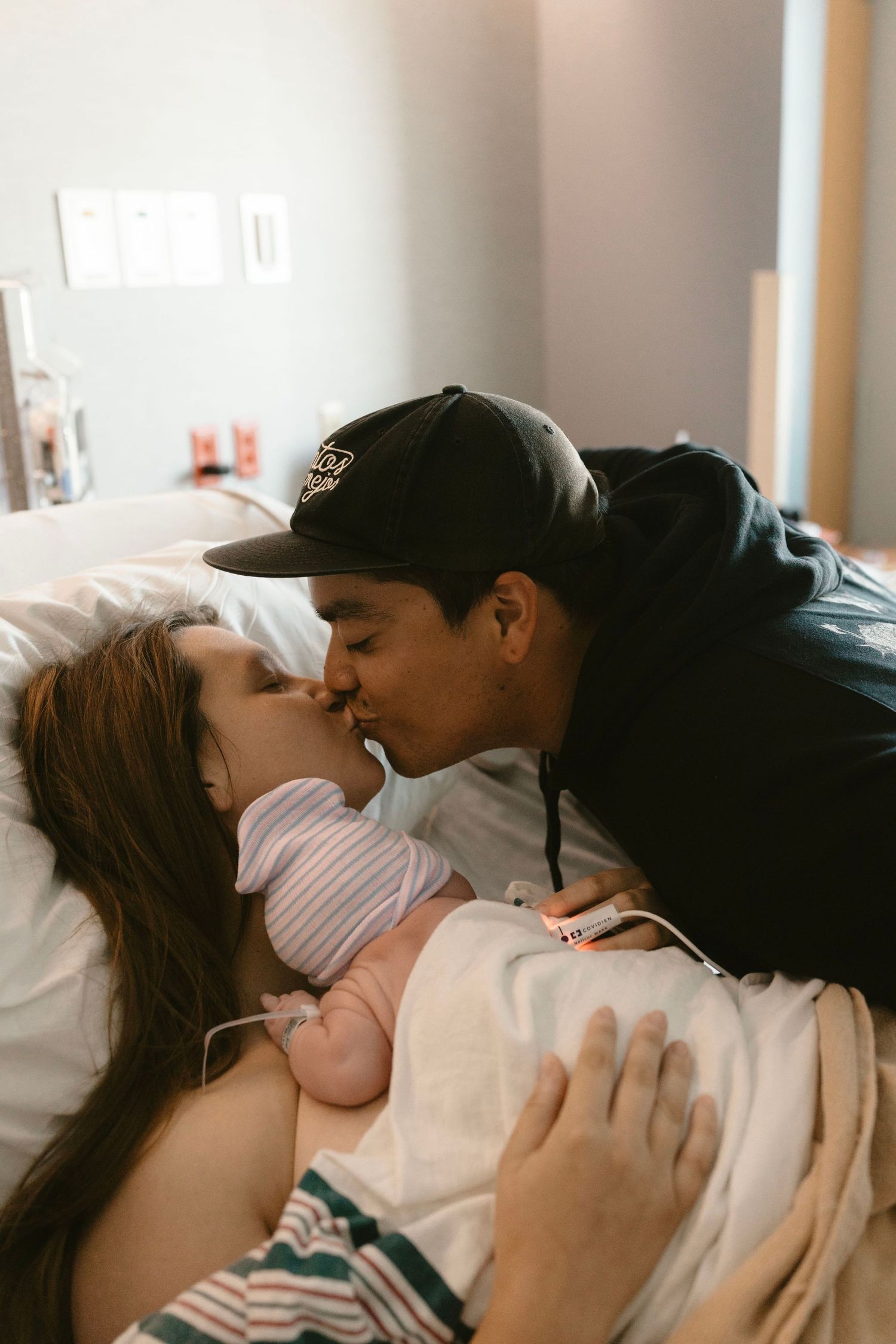 mom holds baby and dad leans in for a kiss.