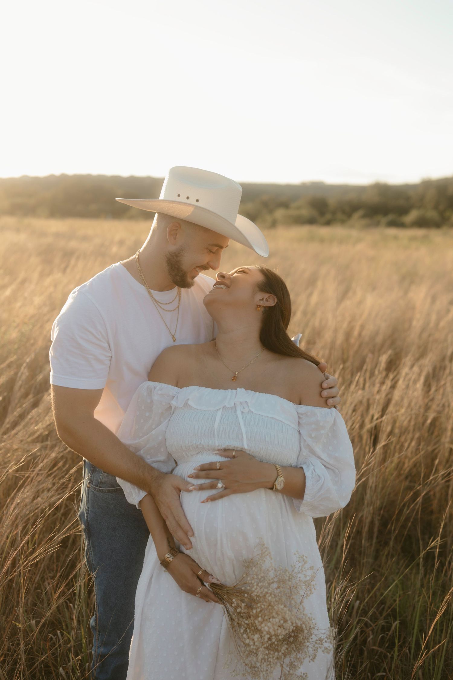 A tender moment between a couple during their maternity photoshoot in a sunlit field of tall grass.