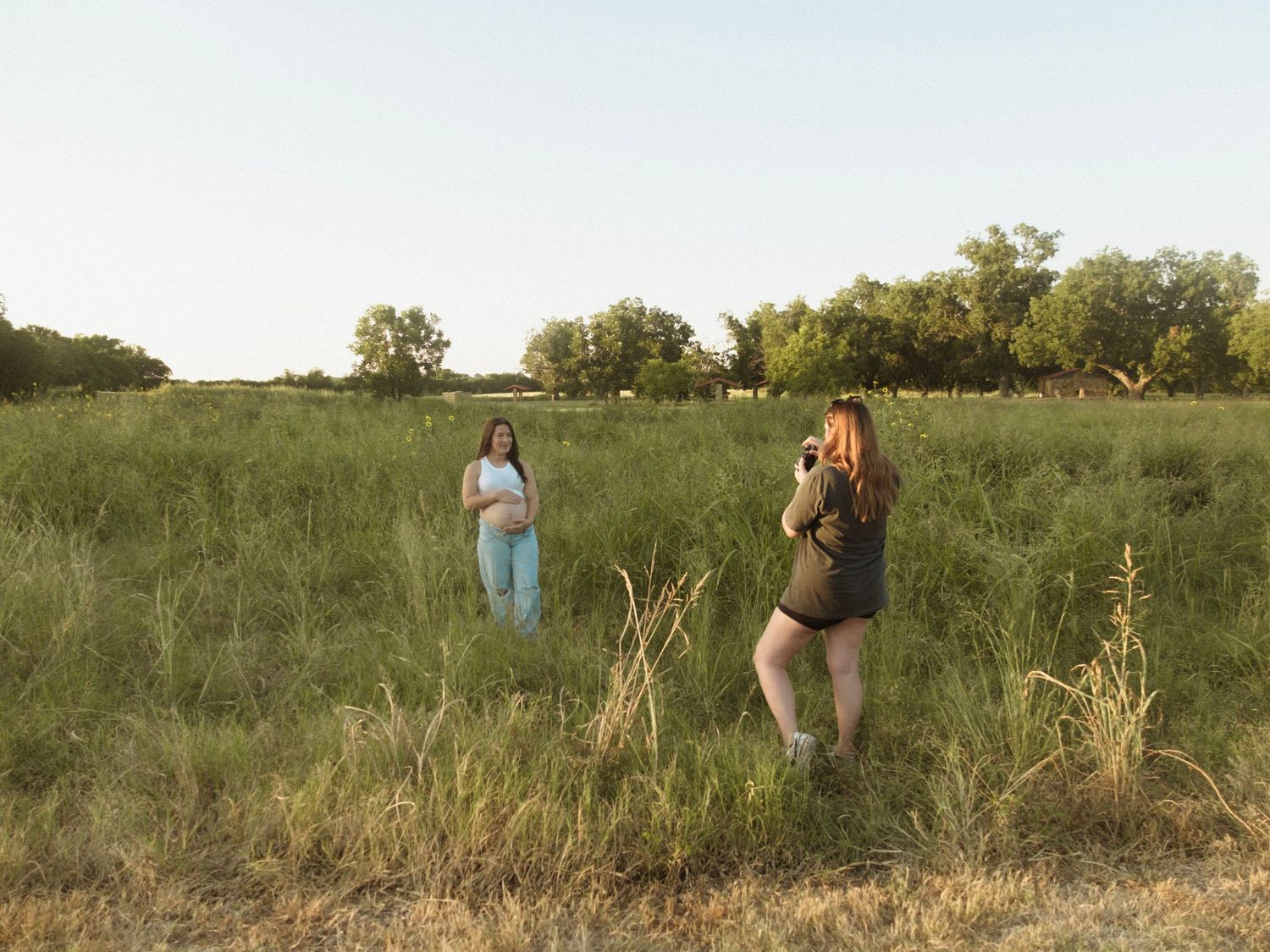 Photographer capturing a maternity session of a pregnant person in an open green field.