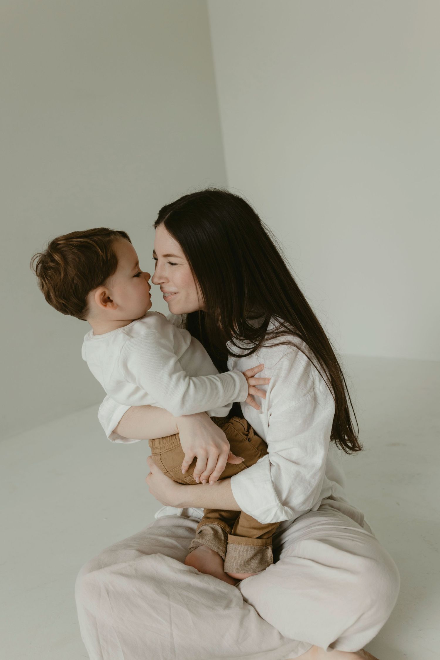 A tender moment captured in white tones showing affectionate interaction between parent and child on neutral background.