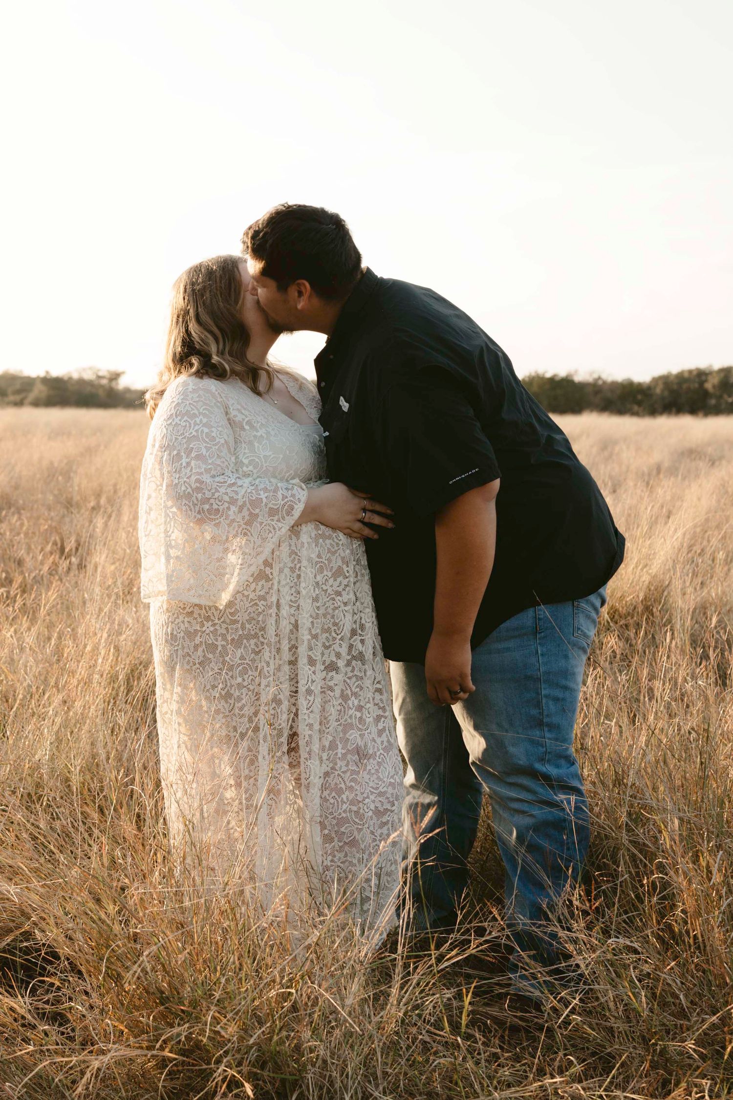 A romantic couple embraces in a golden sunlit field of tall grass during sunset.