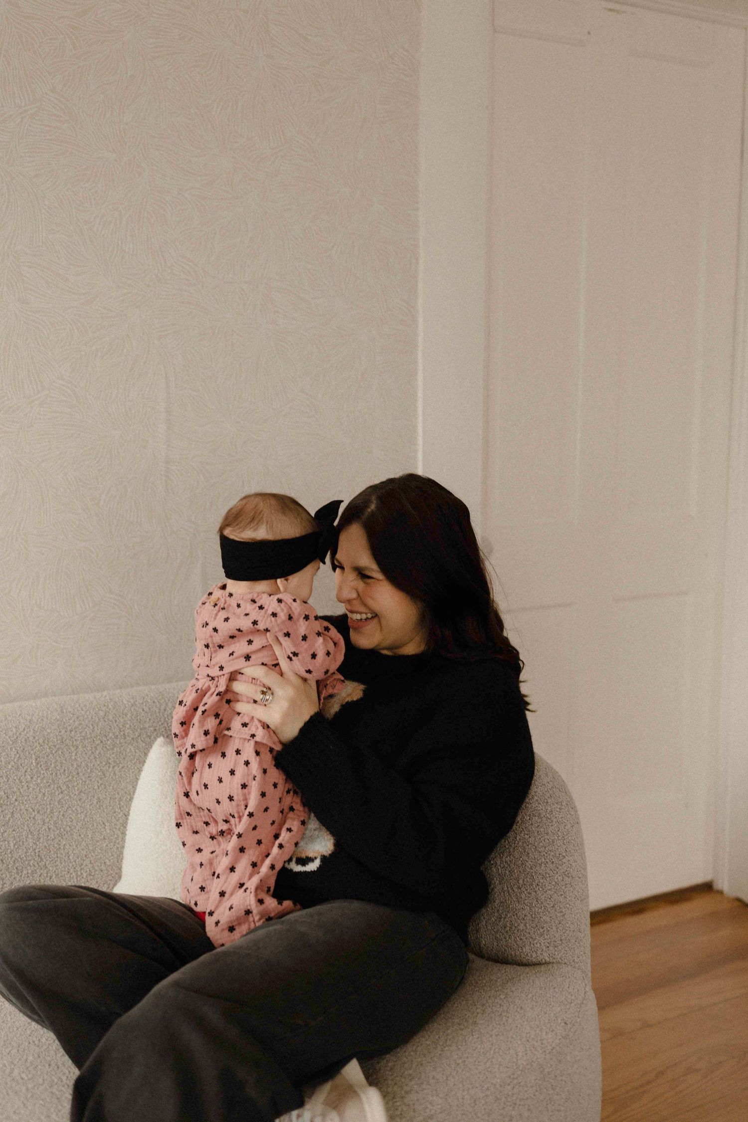 A mom in black clothing rests on a couch looking at her baby
