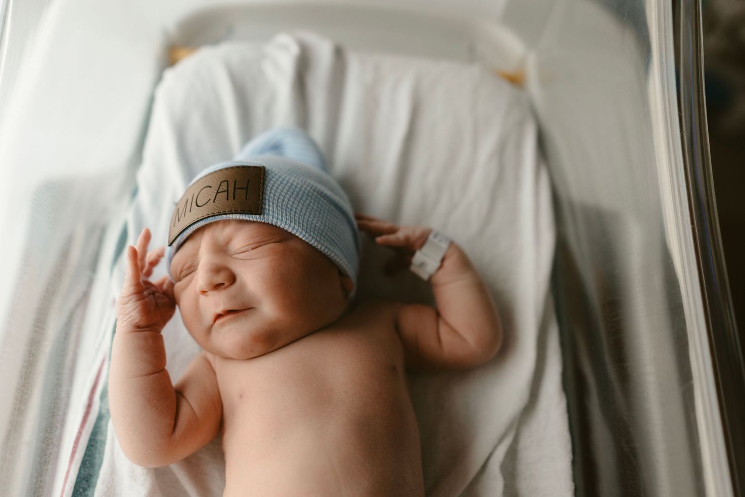 A peaceful photograph by Brittany Ruiz Photography showing a sleeping newborn baby in white blankets and a knit hat.