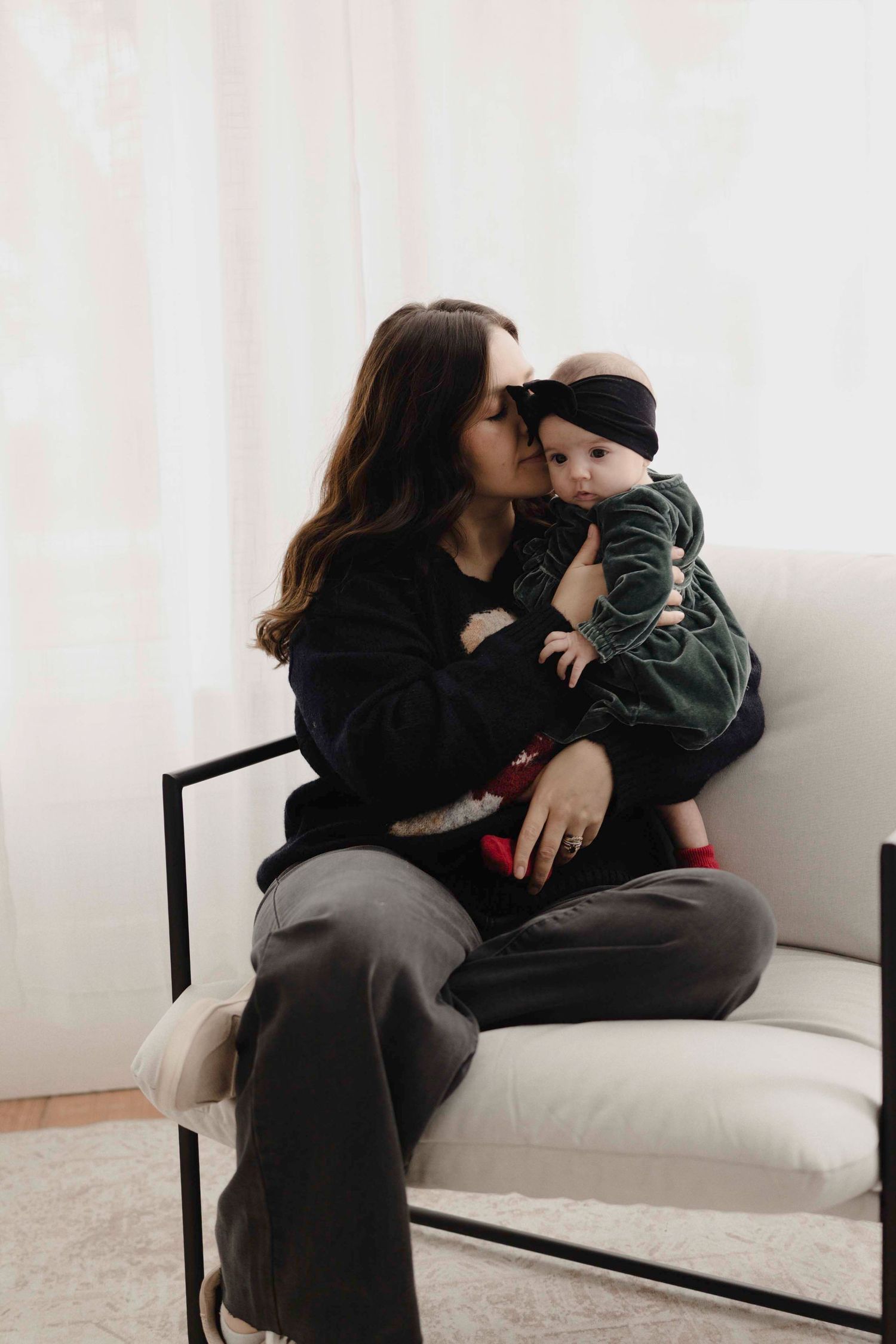 A tender moment shared between two mom and baby together on a white couch in a minimalist room.