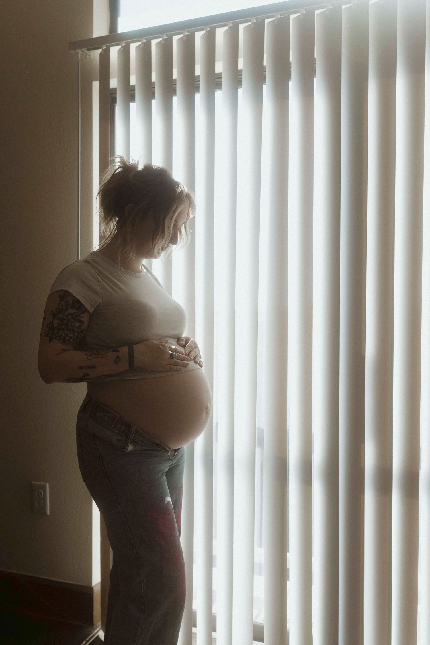 Silhouetted standing pregnant women by vertical window blinds in a dimly lit room.
