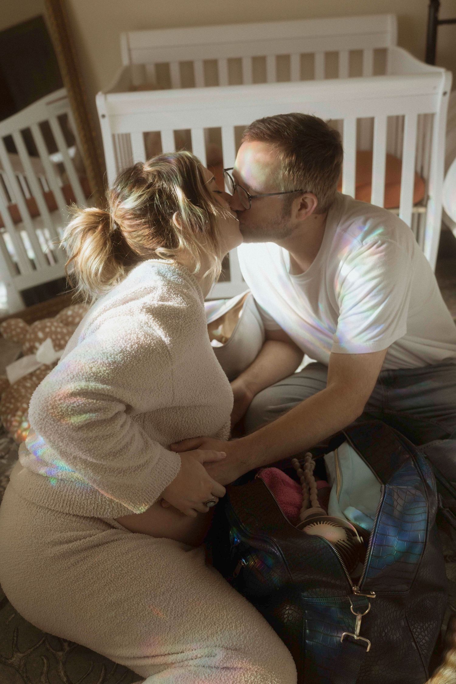 Intimate couple kissing captured in a nursery with white crib.