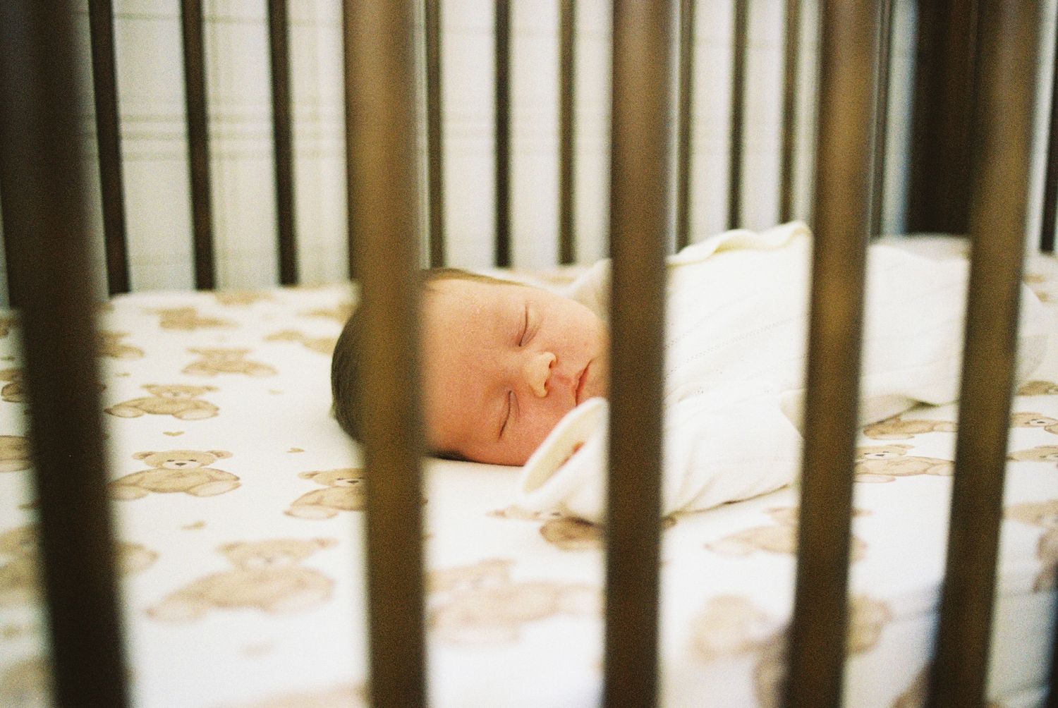 A sleeping baby lies peacefully in a wooden crib with white bedding.