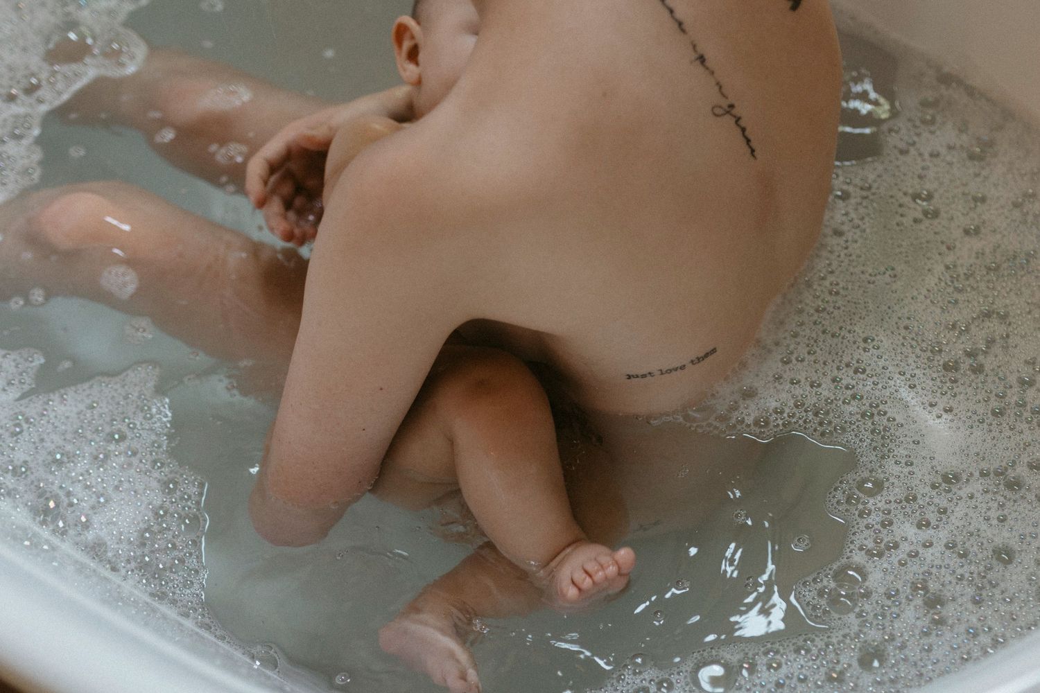 Intimate motherhood photo of a new mom bathing with baby.