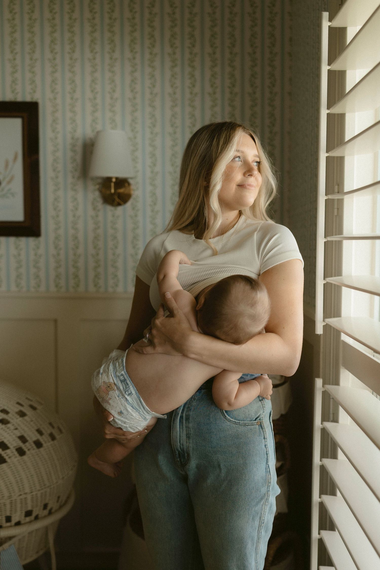 Lifestyle motherhood session showing a mom gently holding her baby in the doorway with natural light.