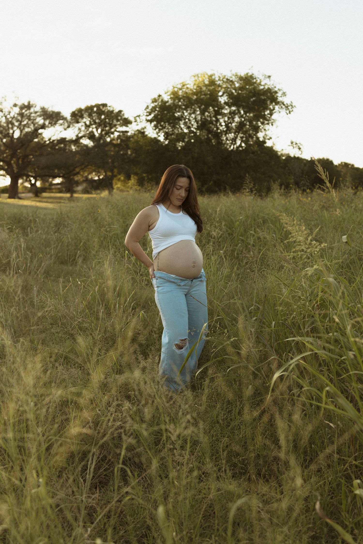 A person searches through tall grass in an outdoor field during golden hour lighting.