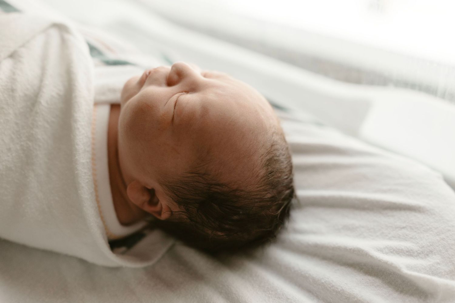 Profile view of sleeping newborn's first moments on crisp white hospital bedding.