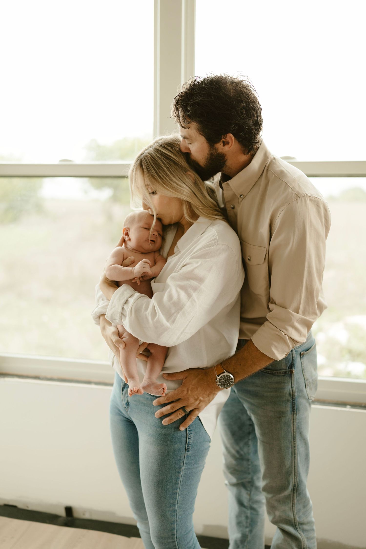 Family sharing an intimate moment together with newborn baby by a bright window in Texas.