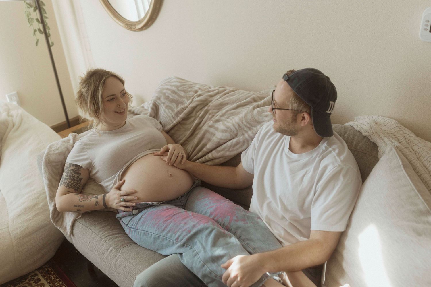 A series of photos showing people relaxing and lounging on white bedding in casual comfortable clothing, touching pregnant belly