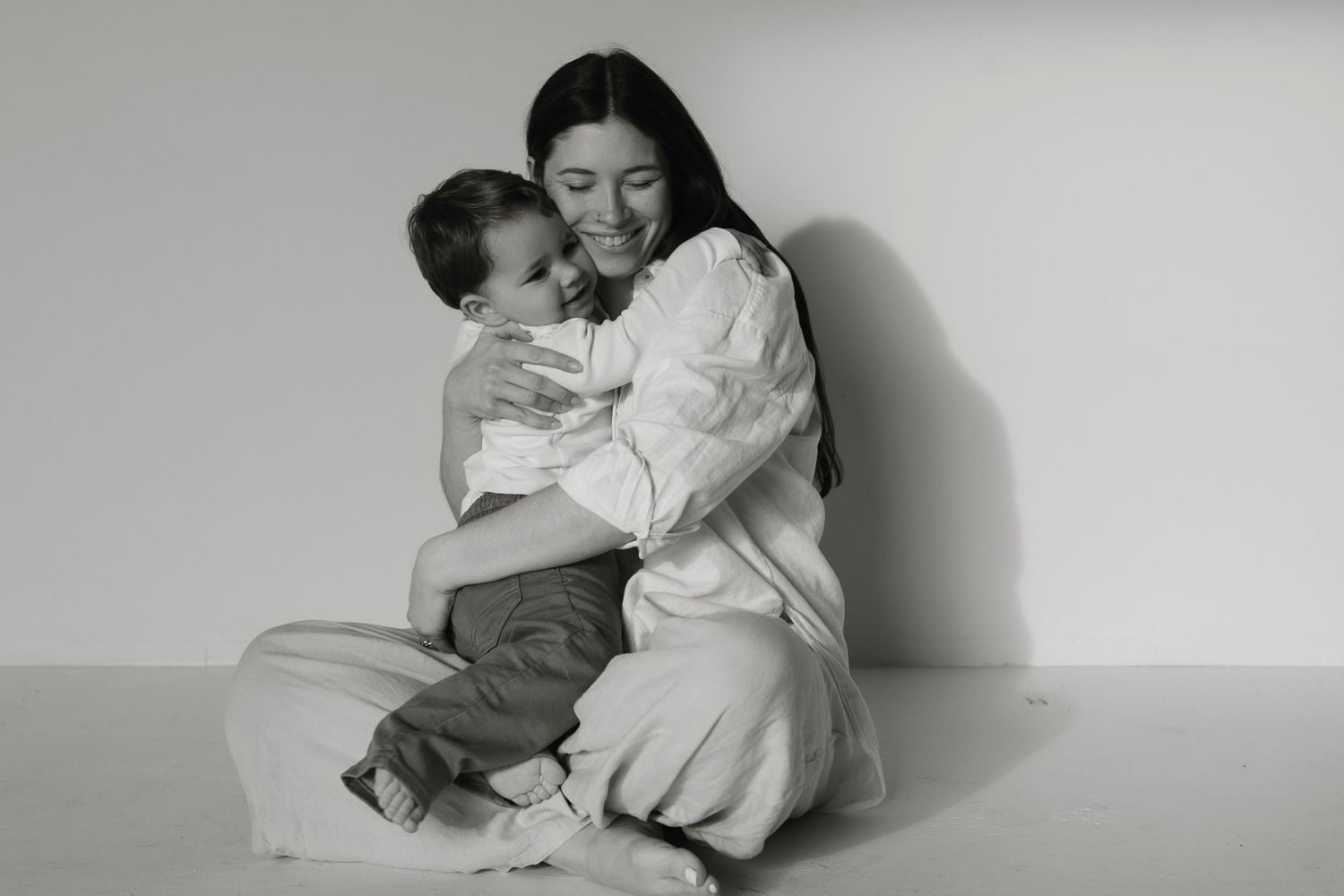 A series of black and white photographs showing tender moments between parent and child in a minimalist setting.