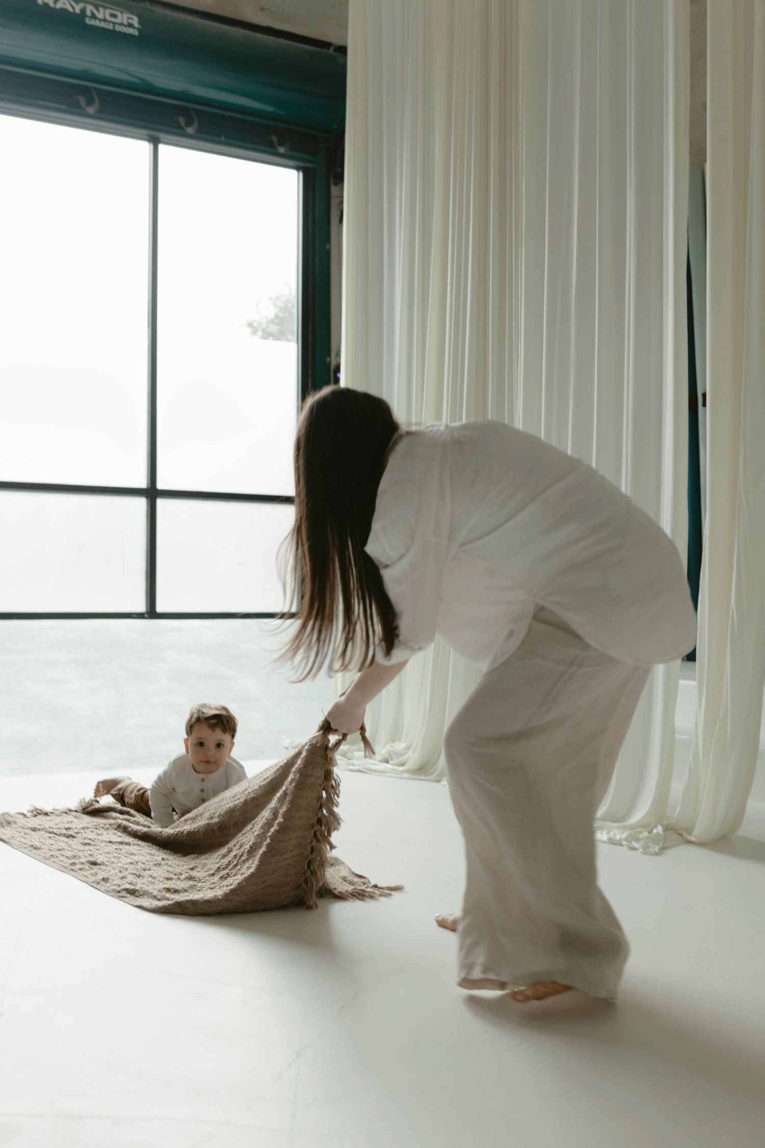 Documentary-style motherhood session of a mom and son sharing playful moments in a clean white studio.