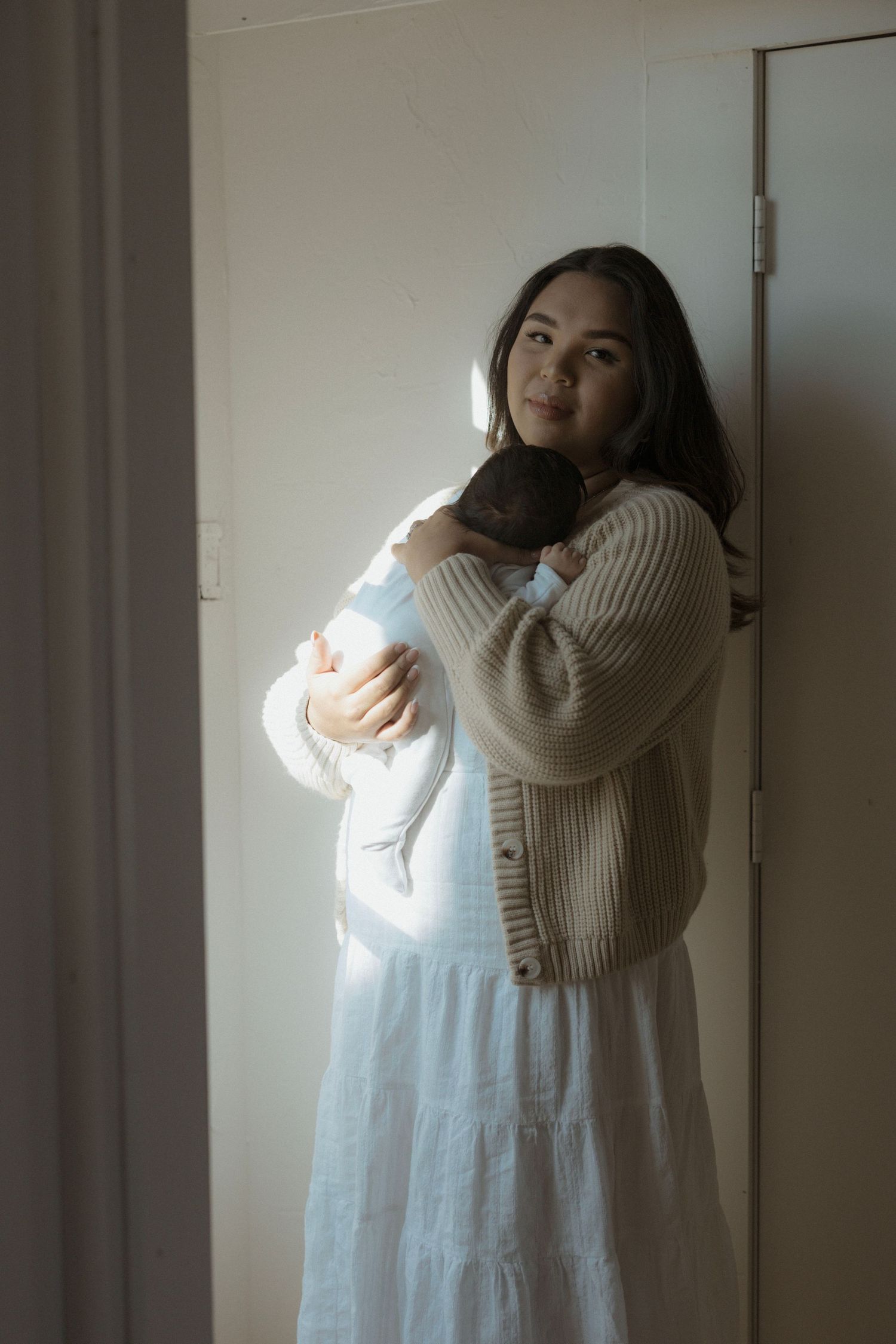 Cozy newborn photo with mother in dress and cardigan.