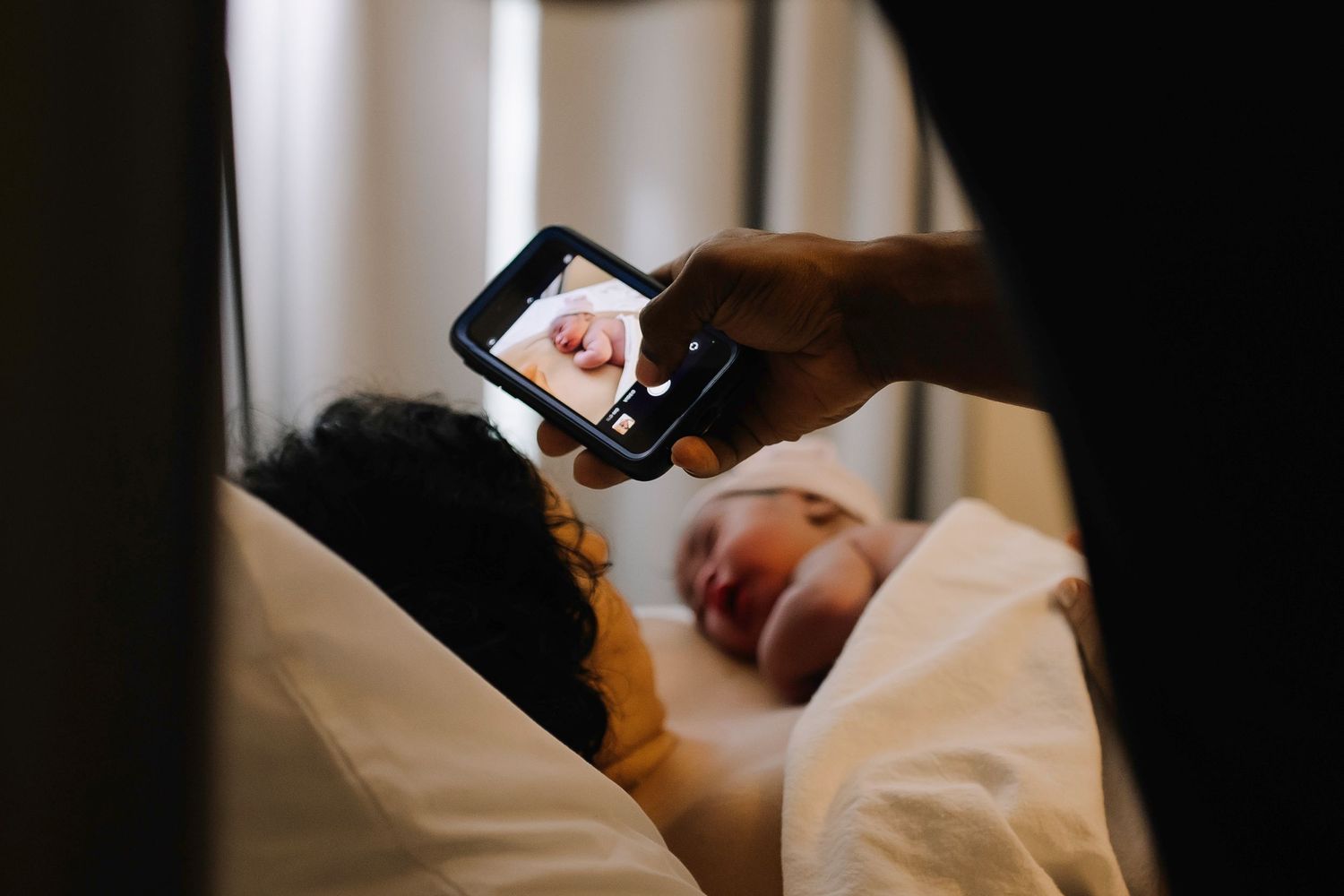 Candid birth image of a dad taking photos of mom and newborn shortly after birth.