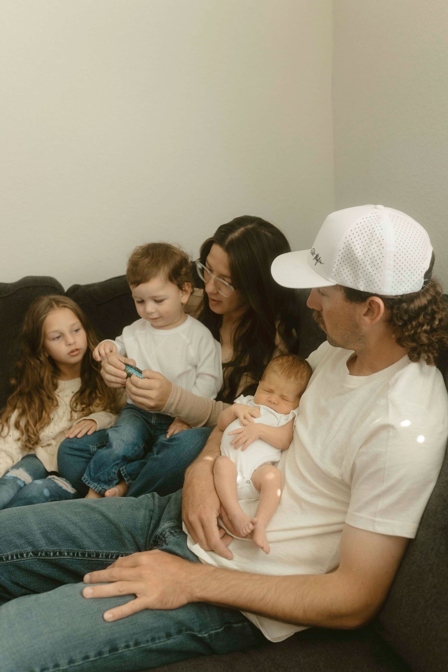 A family sits together on a couch sharing a tender moment with their young children.