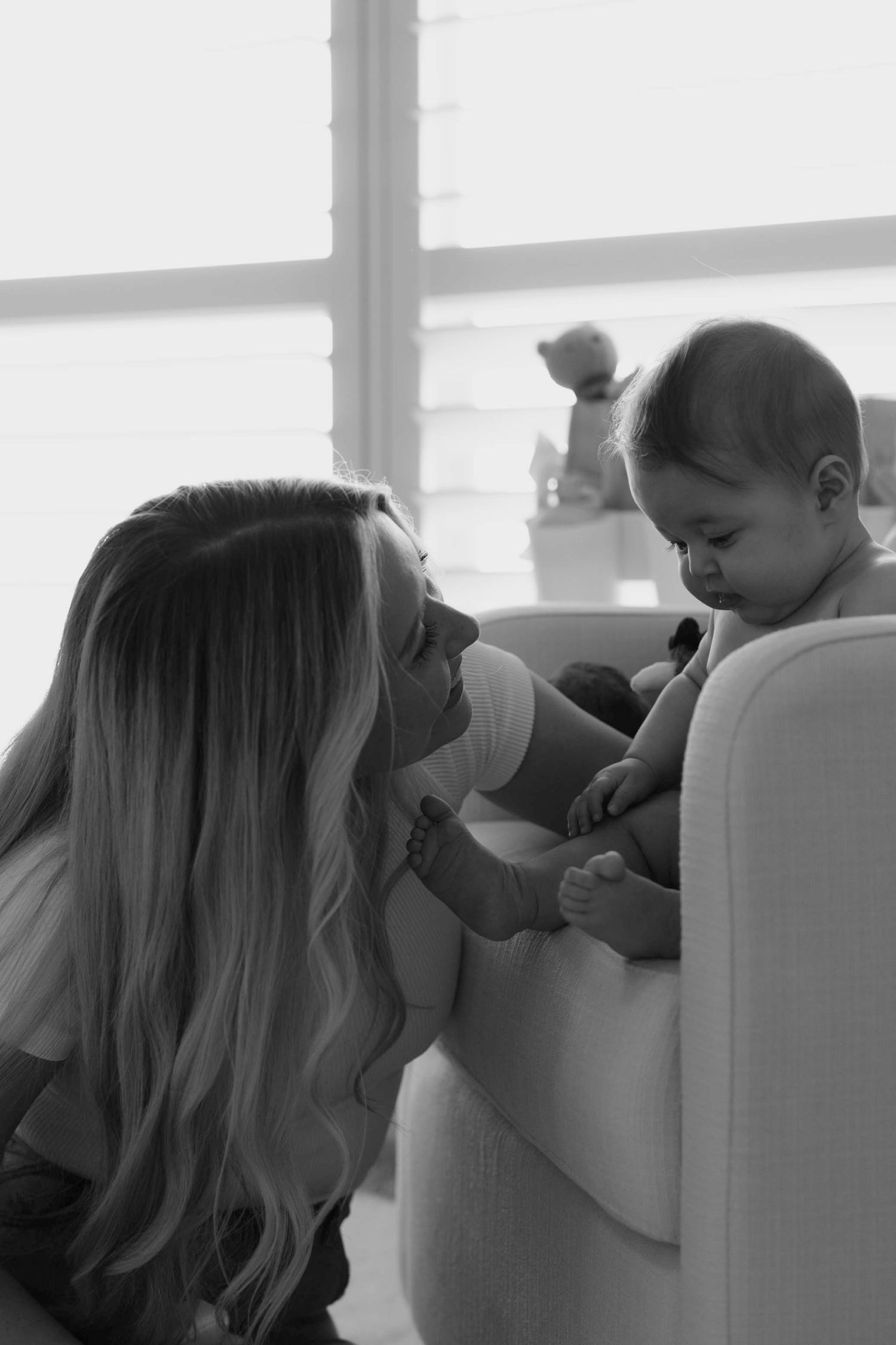 A tender black and white moment between parent and baby sitting in a chair by a window.