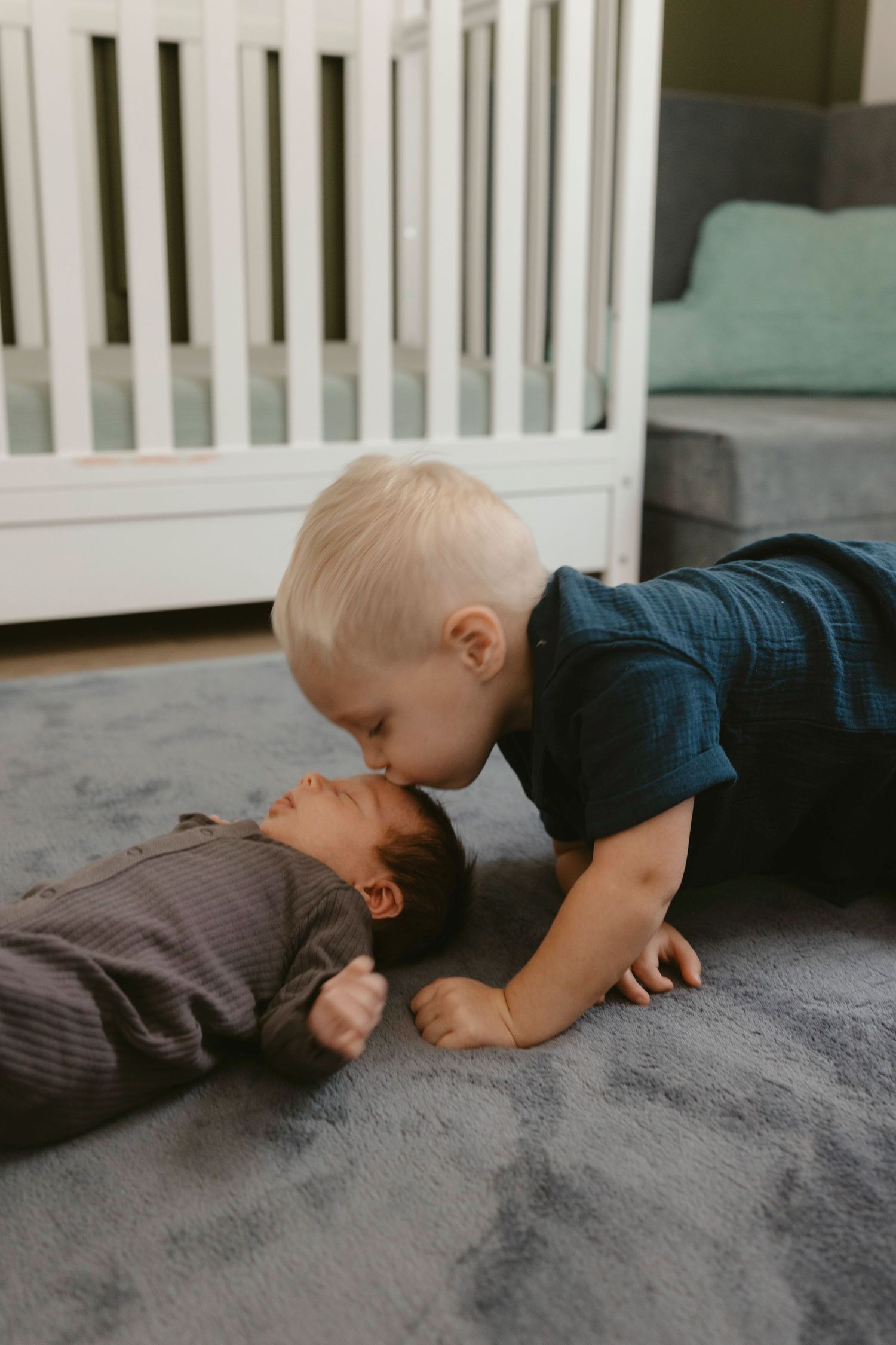 big brother kissing his newborn sibling on the ground